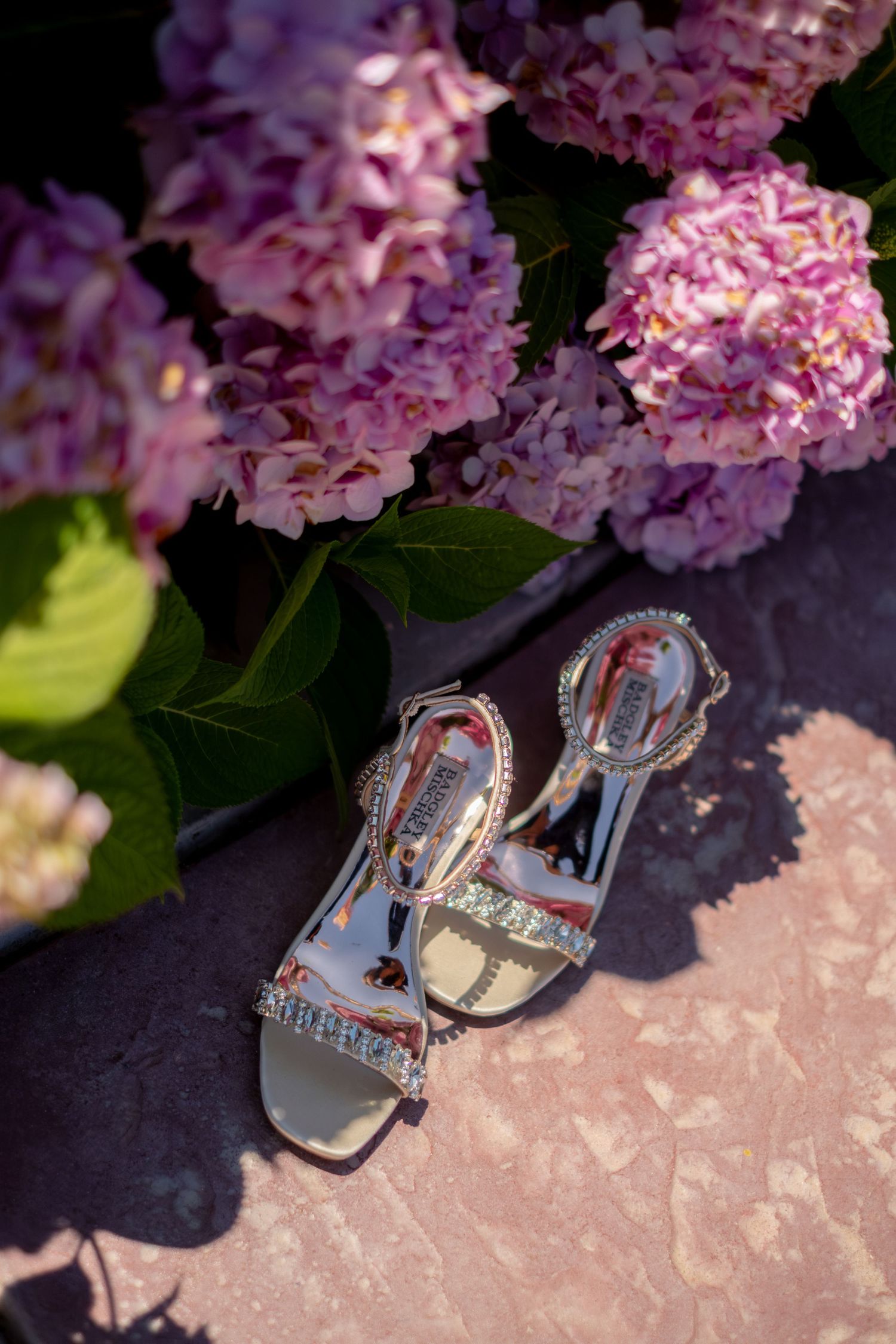 Silver crystal wedding sandals displayed beside pink hydrangea flowers.