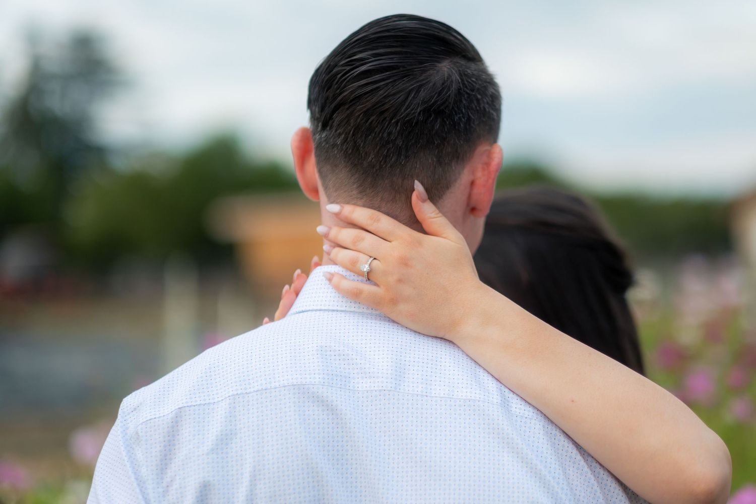Close-up of bride's diamond engagement ring resting on groom's neck outdoors.