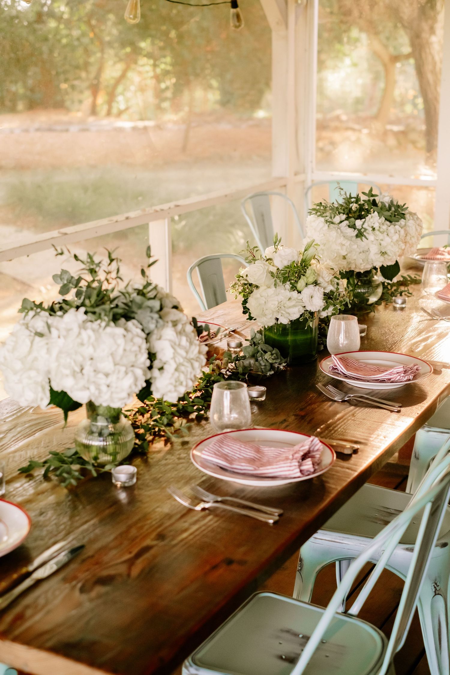 Elegant rustic wedding tablescape with white hydrangeas, pink plates, and greenery in tent.