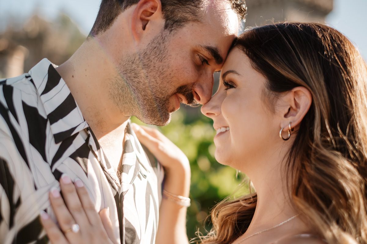 Romantic couple sharing an intimate moment, touching foreheads and smiling at each other outdoors.