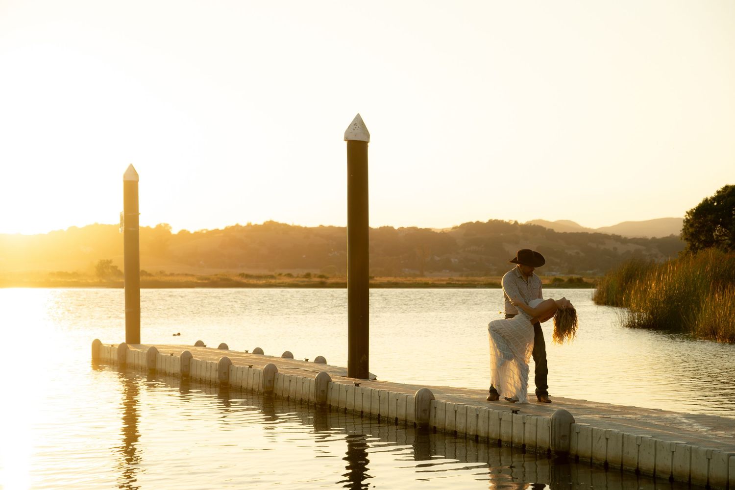 Couple sharing a romantic embrace on a dock at golden hour with a serene lake backdrop.