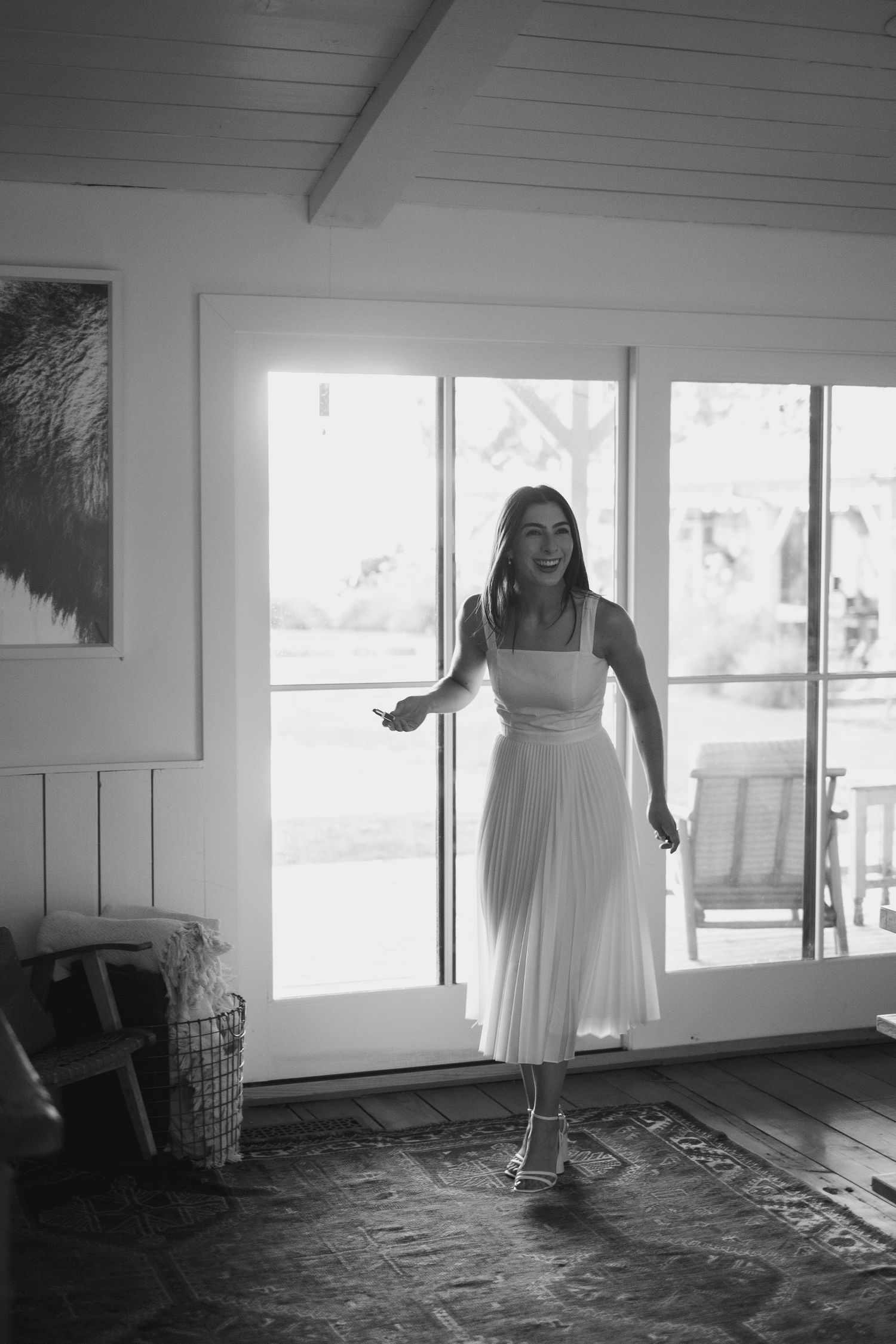 Bride twirling in elegant white midi dress, laughing joyfully in black and white wedding photo.