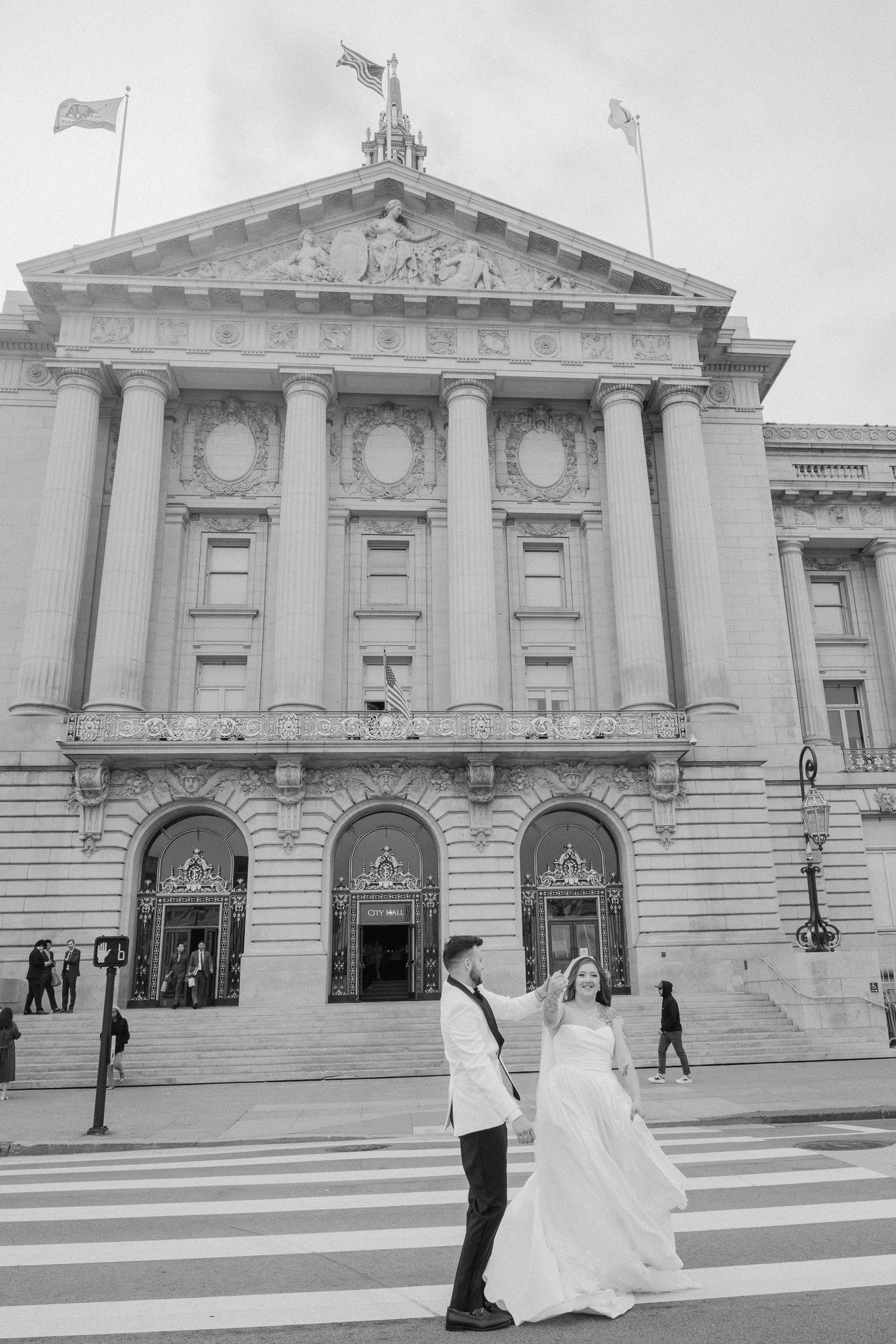 Black and white photo of bride and groom crossing street before grand city hall.