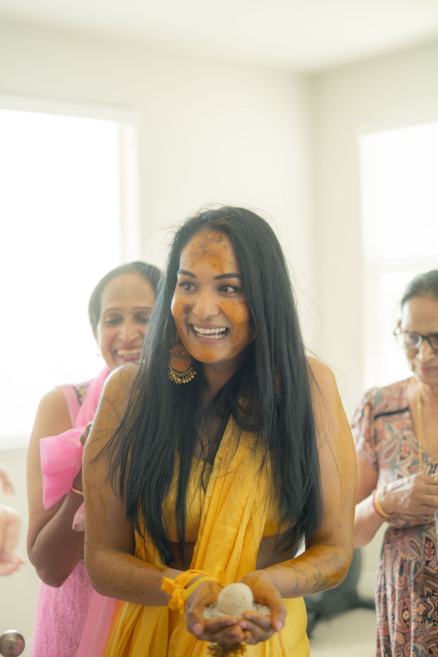 Young Indian woman smiles with turmeric on her face during a Haldi ceremony.
