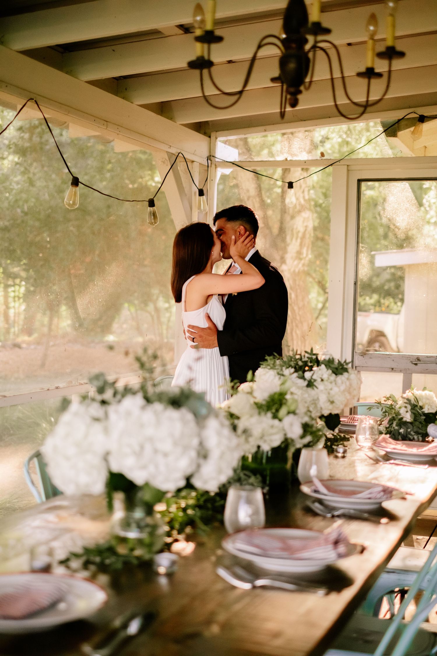Couple sharing a kiss at decorated reception table with white floral centerpieces.