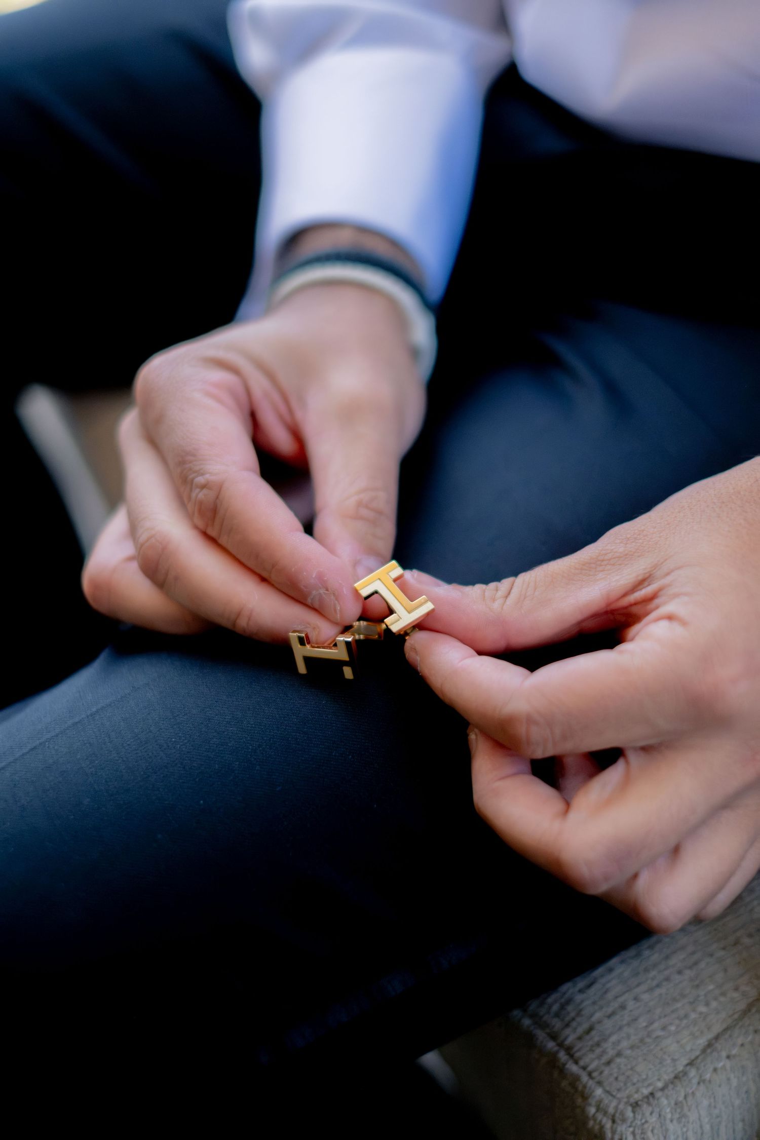 Close-up of hands fastening gold Hermes cufflinks on a white dress shirt sleeve before a wedding.
