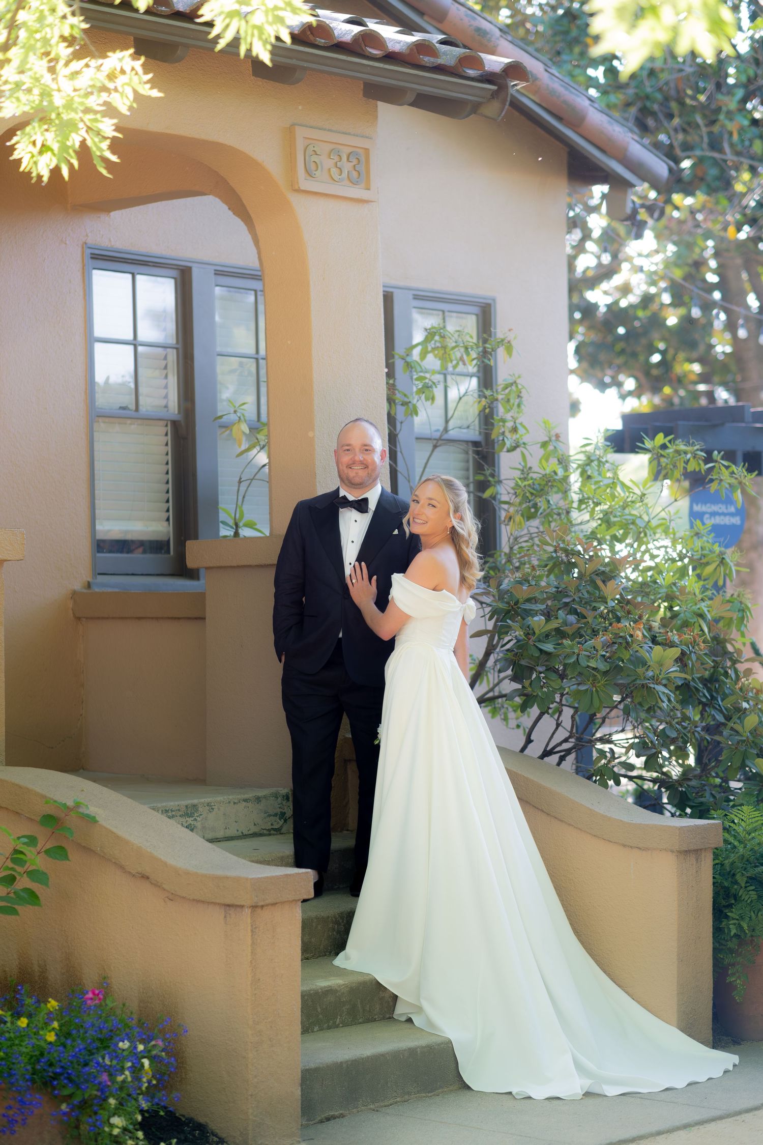 Bride and groom posing on steps of building 633, bride in flowing off-shoulder gown and groom in black tuxedo.