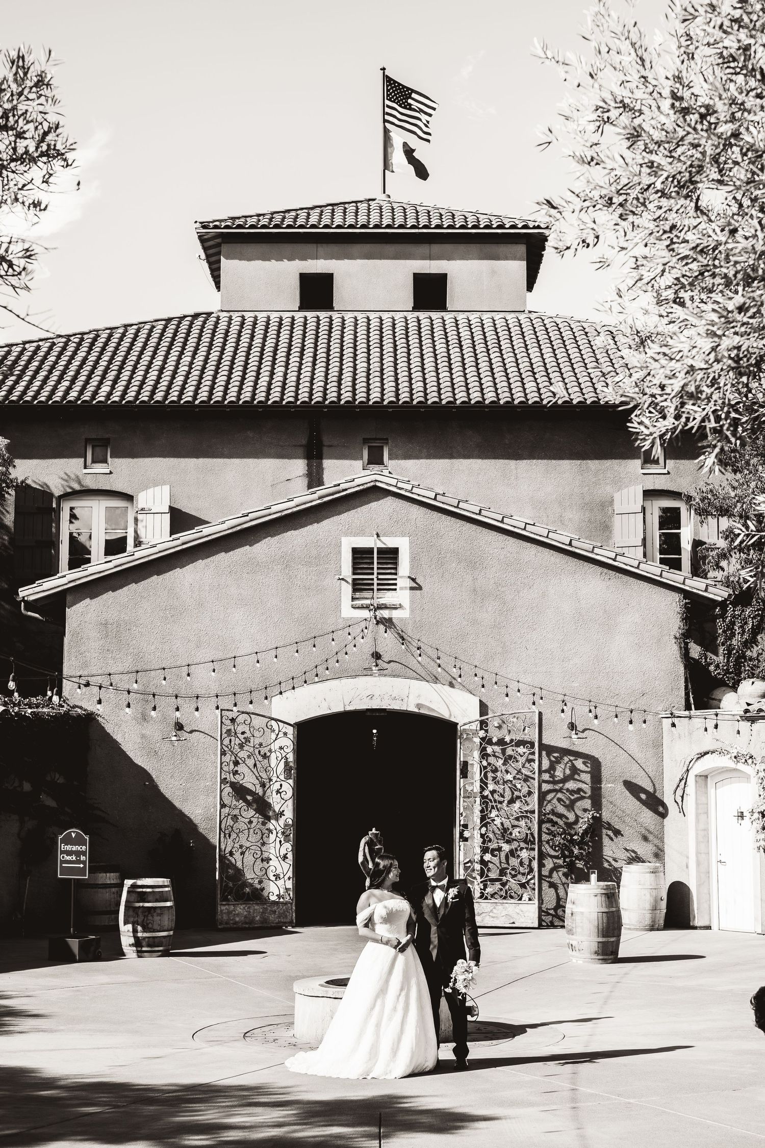 Bride and groom walk in front of a rustic winery building in a black and white wedding photo.