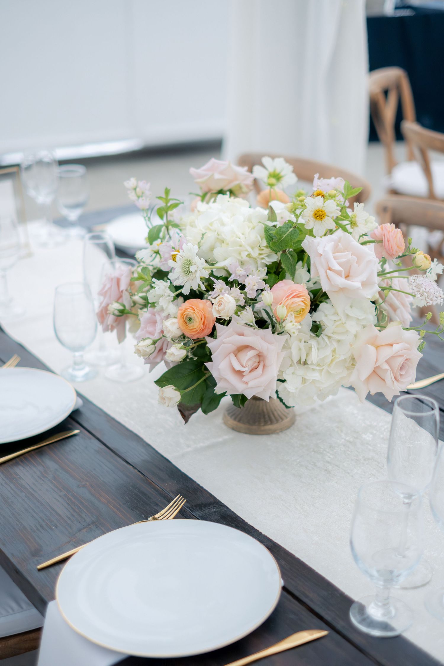 Elegant wedding table centerpiece with blush roses, white hydrangeas, and gold cutlery on dark wood.