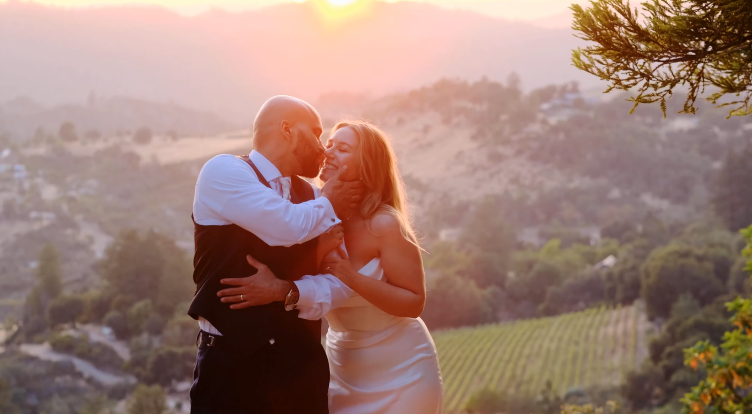 Couple shares a tender kiss at sunset with vineyard valley views in the golden background.