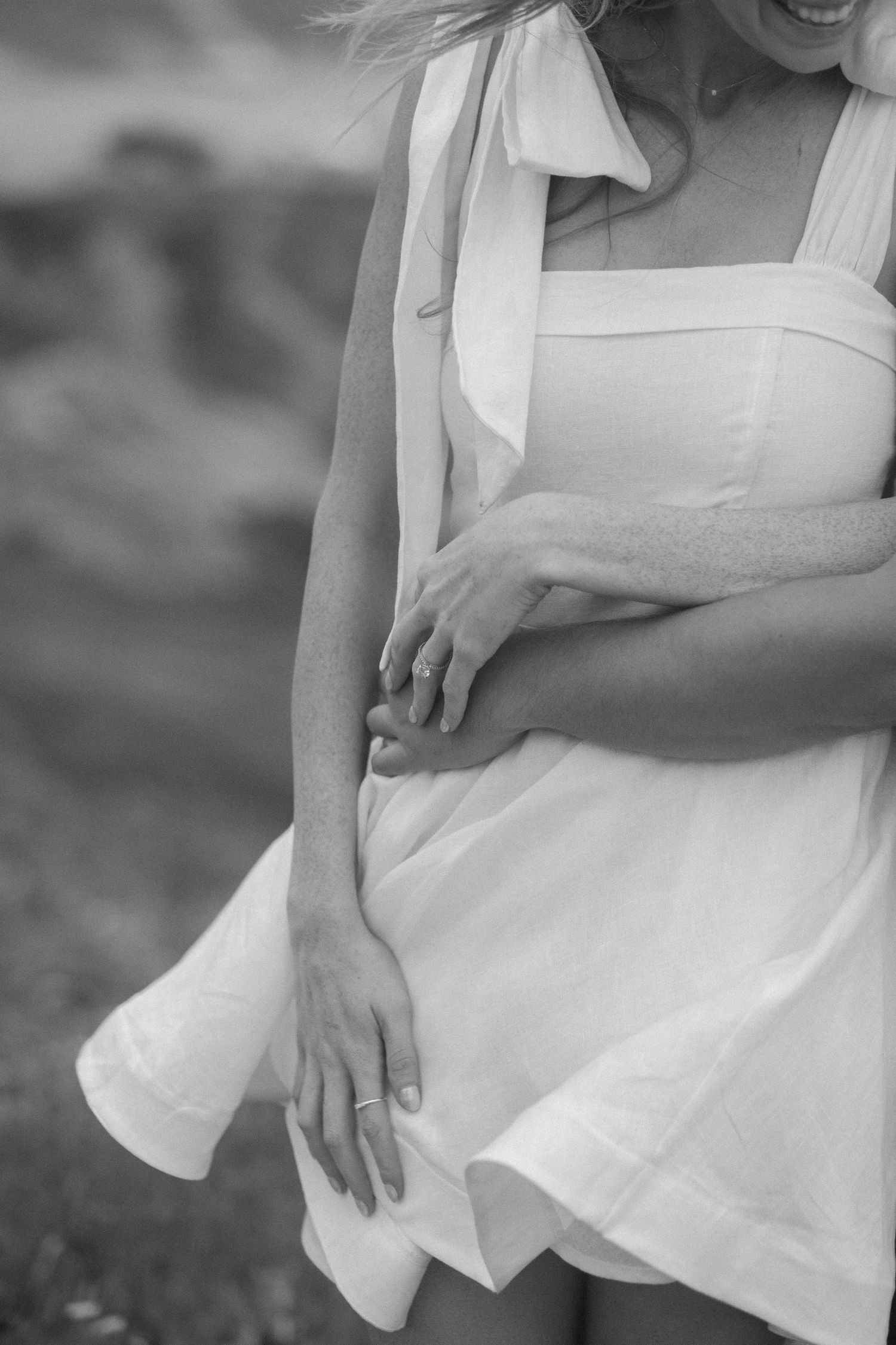 Black and white close-up of a woman in a flowing white sundress with tied shoulder straps outdoors.