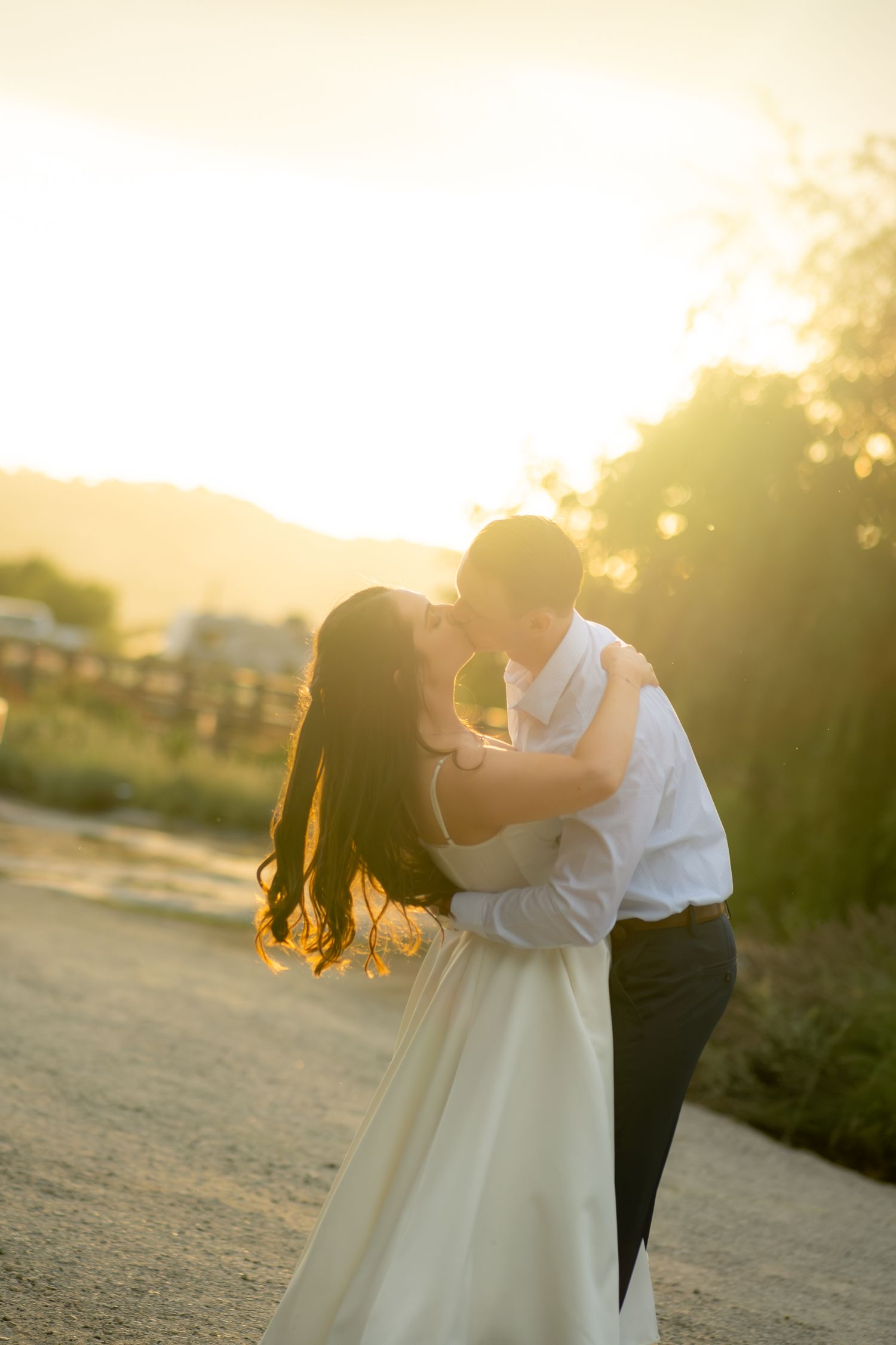 Bride and groom sharing a kiss at golden sunset on a scenic dirt road.