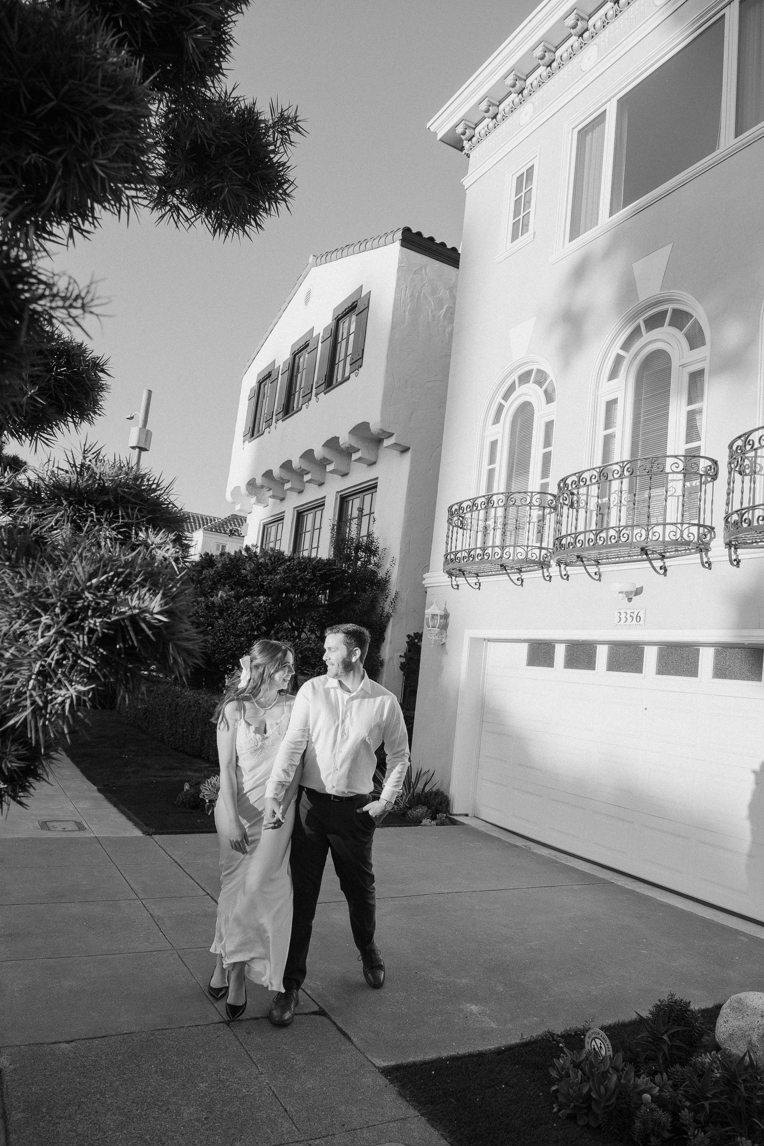 Couple walking hand in hand past elegant Spanish Colonial Revival architecture in black and white photo.