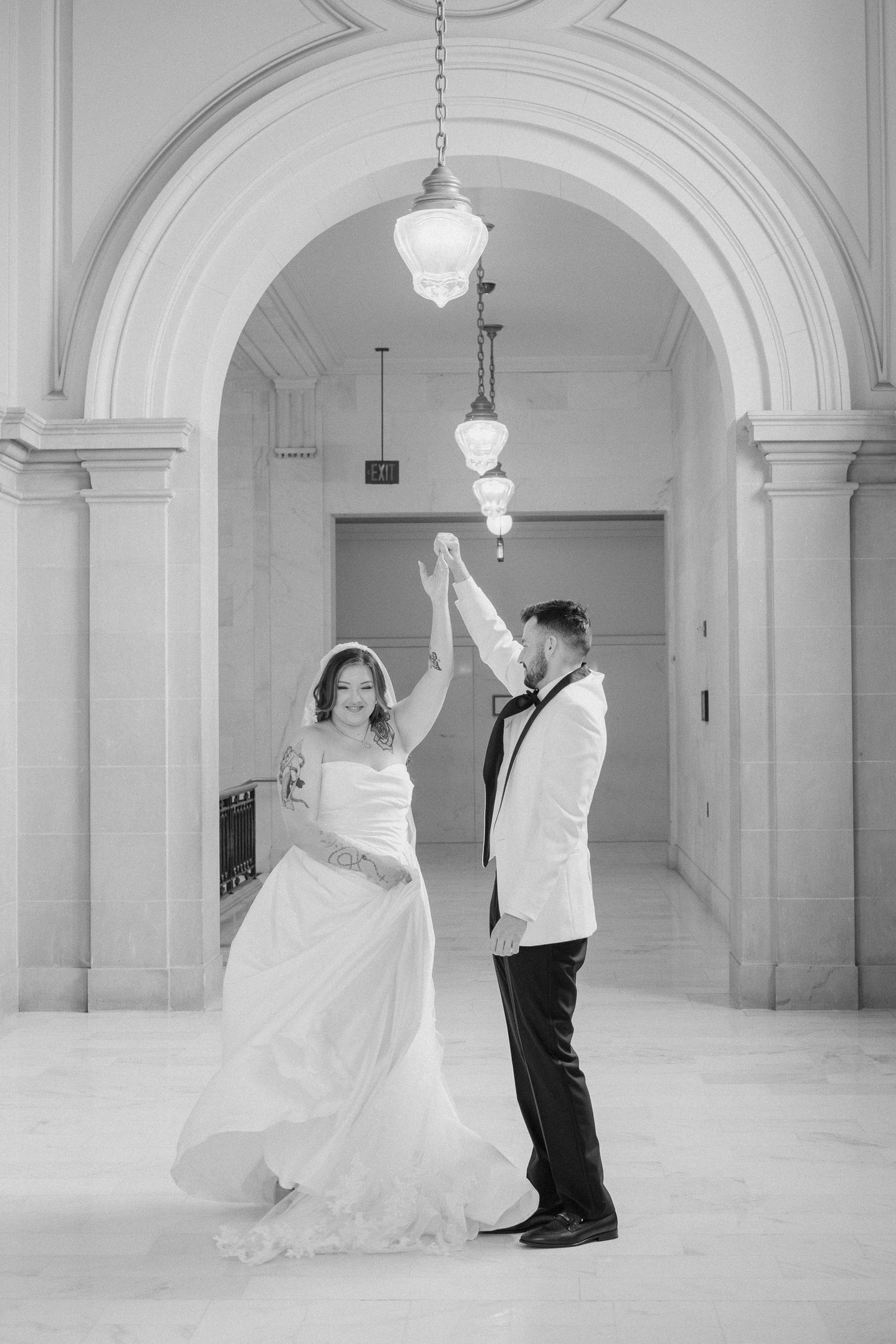 Bride and groom dancing under elegant arched hallway in black and white wedding photo.