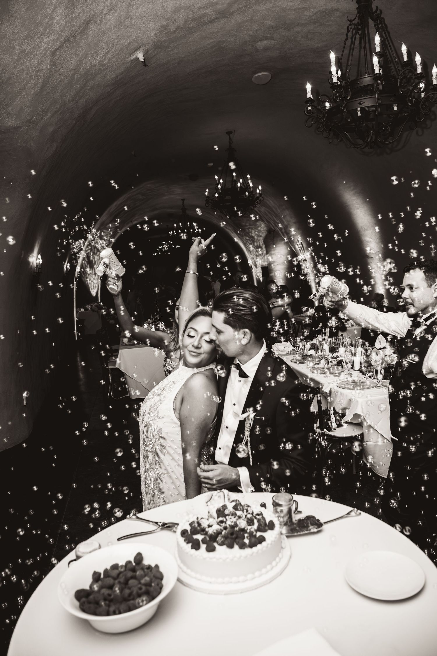 Black and white photo of bride and groom celebrating with confetti in a romantic candlelit cave reception.