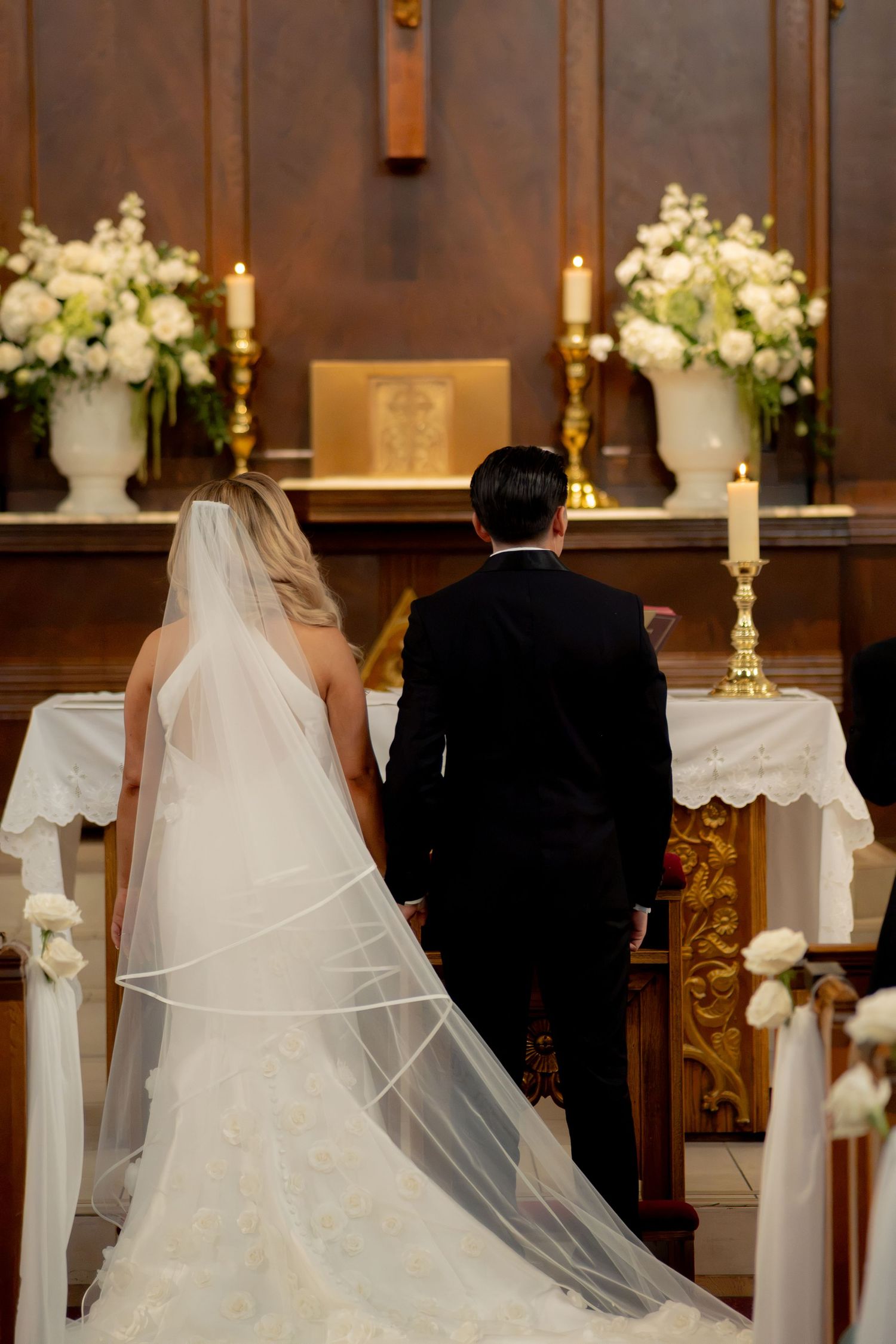 Bride and groom standing at church altar during wedding ceremony with white floral arrangements.