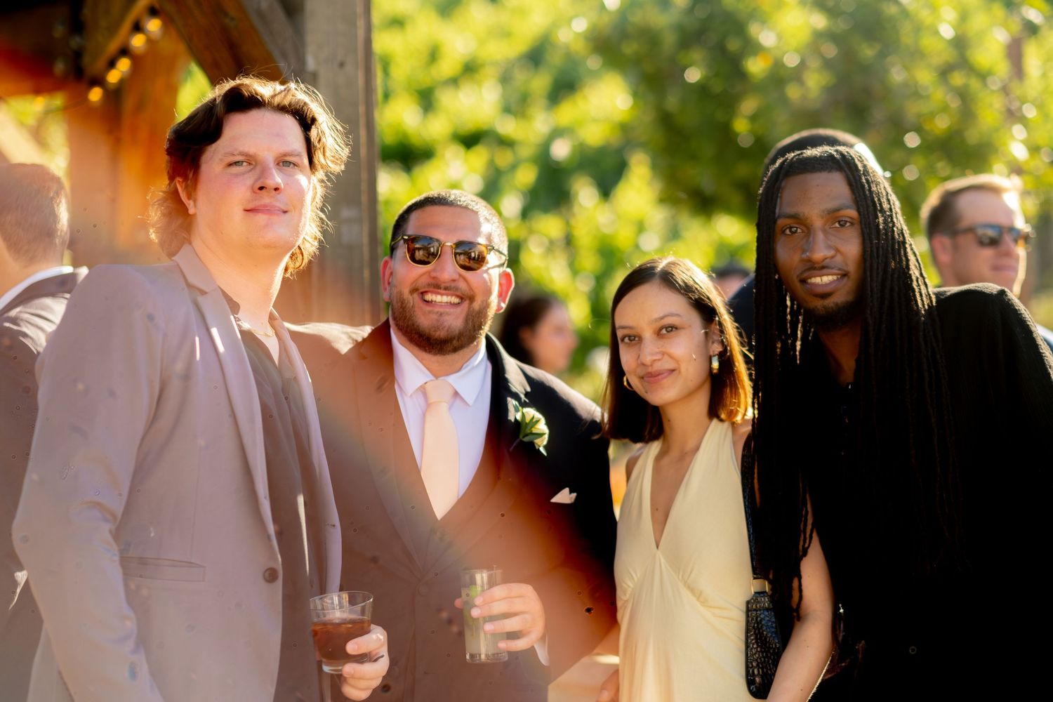 Four wedding guests smile together outdoors during a warm golden-hour wedding cocktail hour.