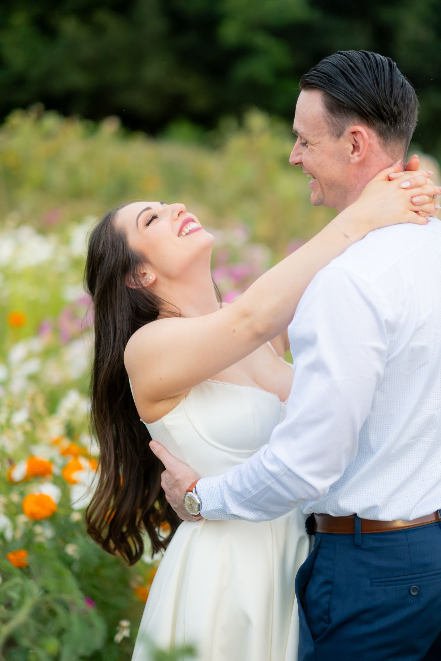 Joyful bride laughing with groom while embracing in a colorful wildflower garden.