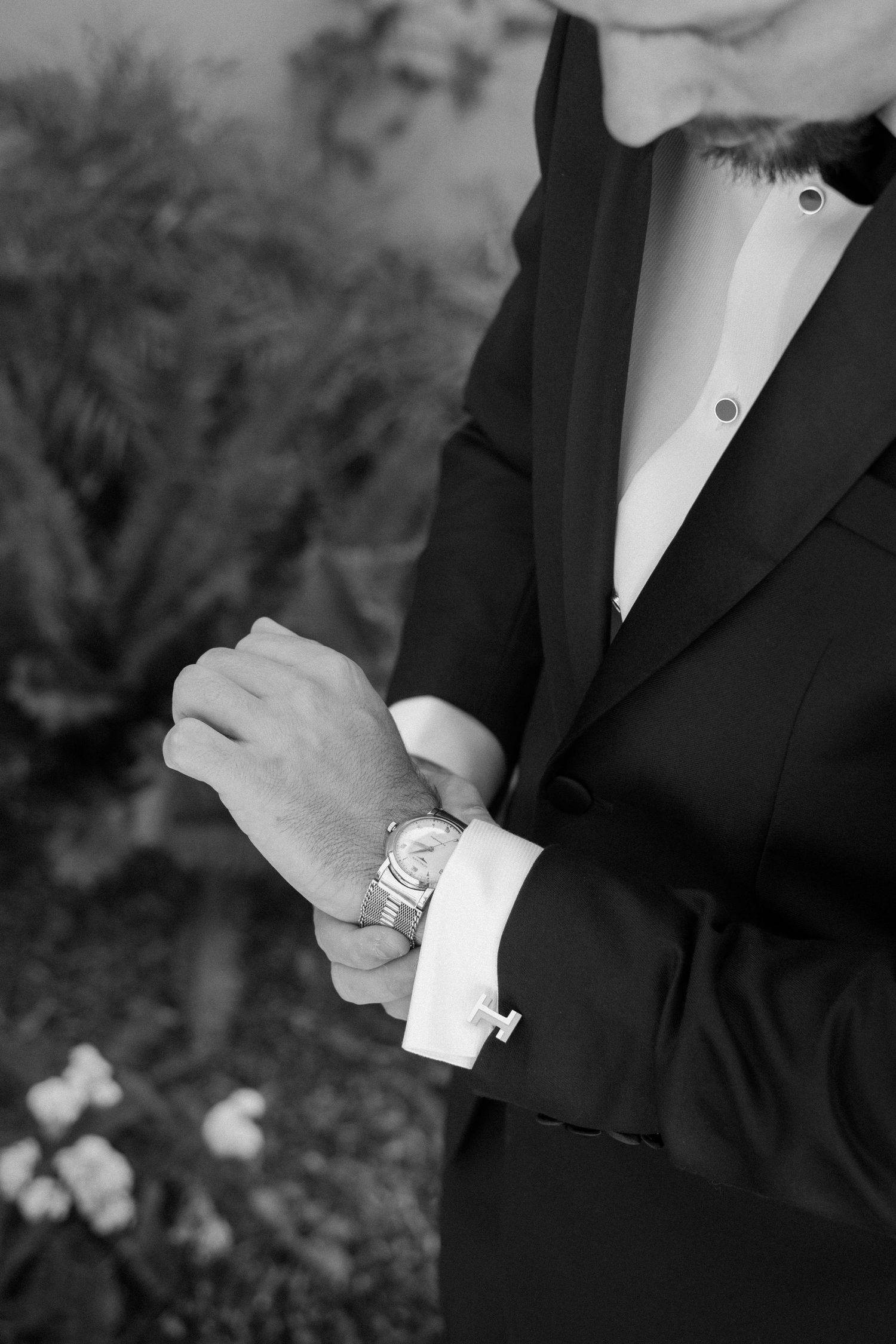 Close-up black and white photo of a groom adjusting his luxury watch and cufflinks before the wedding.