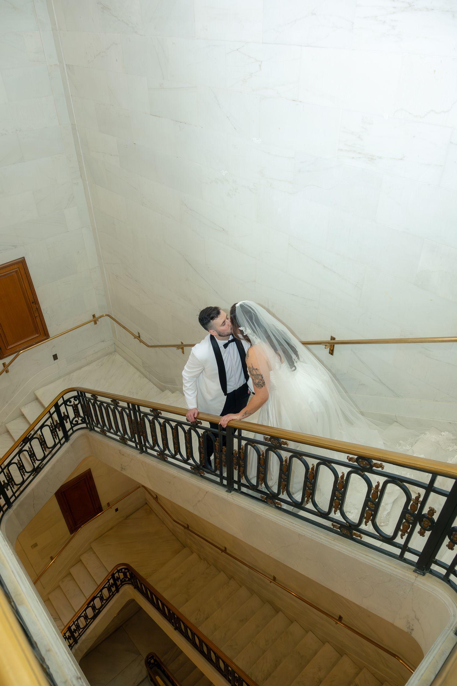 Bride and groom sharing a romantic moment on an elegant marble staircase with ornate iron railings.