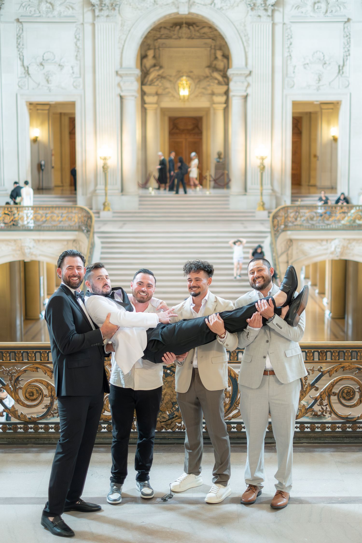 Groomsmen playfully lift the groom inside the ornate San Francisco City Hall rotunda.