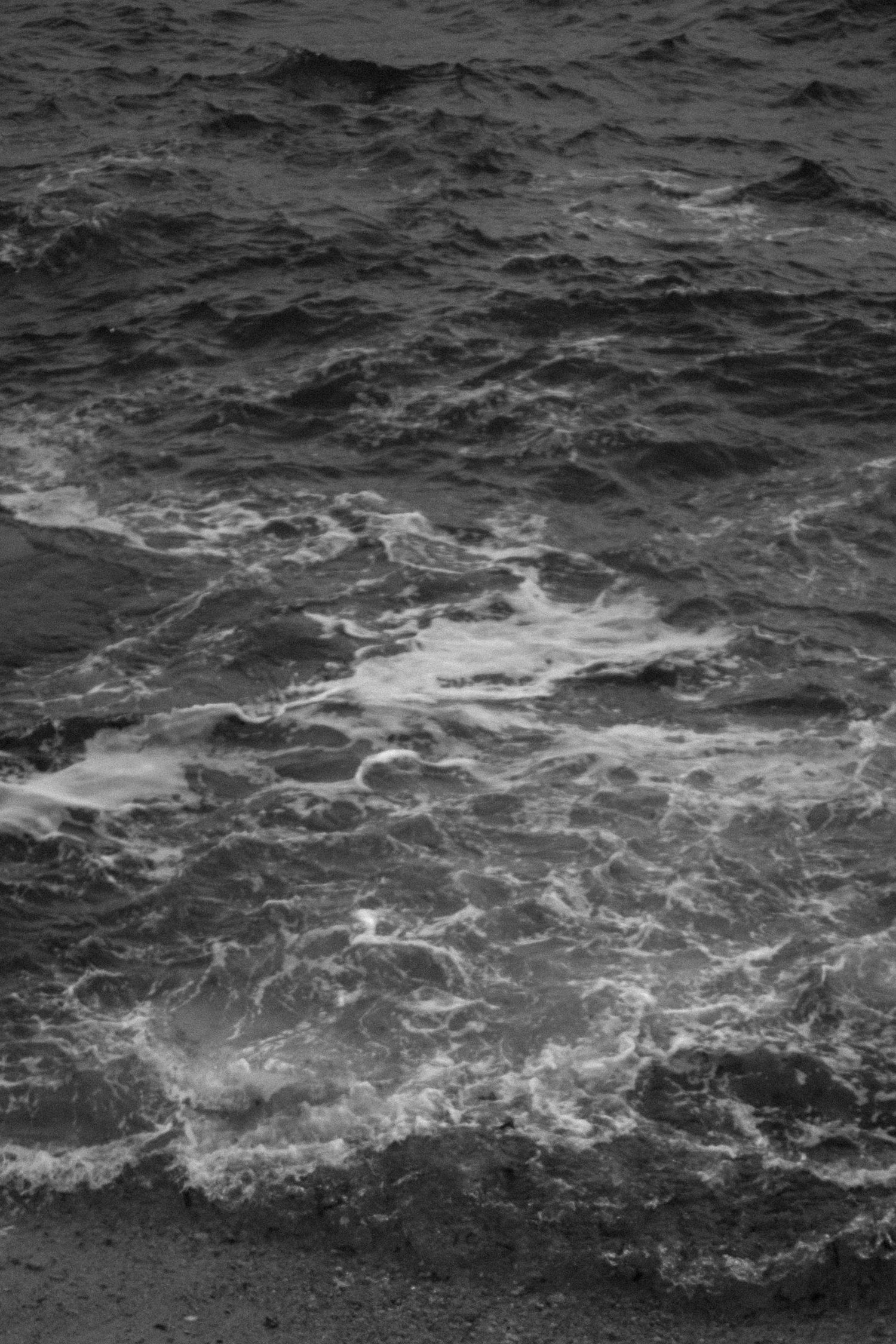Black and white photo of ocean waves crashing on a rocky shoreline.