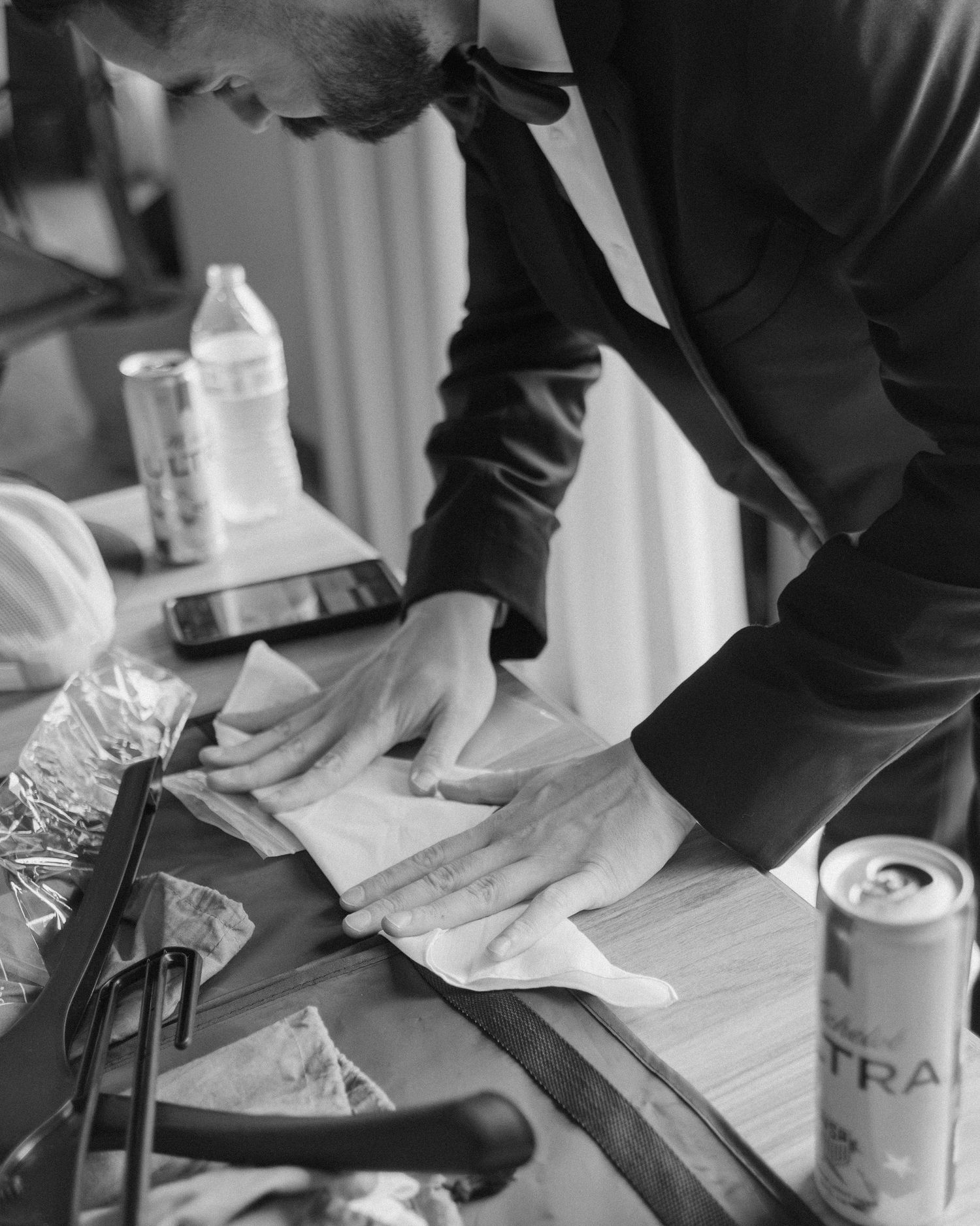 Black and white photo of groomsman carefully preparing boutonniere on table before wedding ceremony.