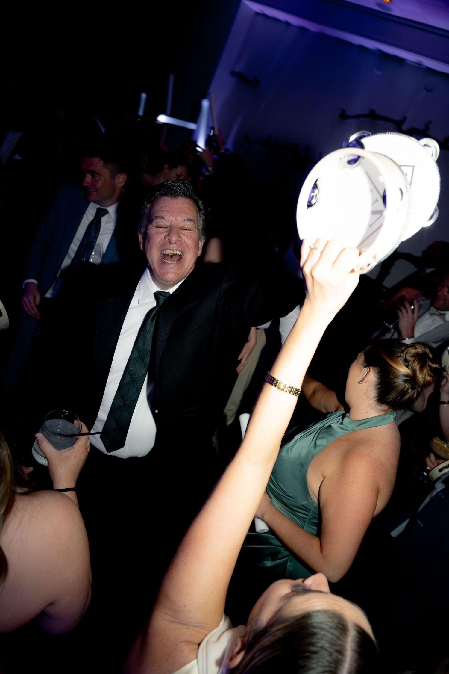 Wedding guest laughing and dancing with tambourine at lively indoor wedding reception party.