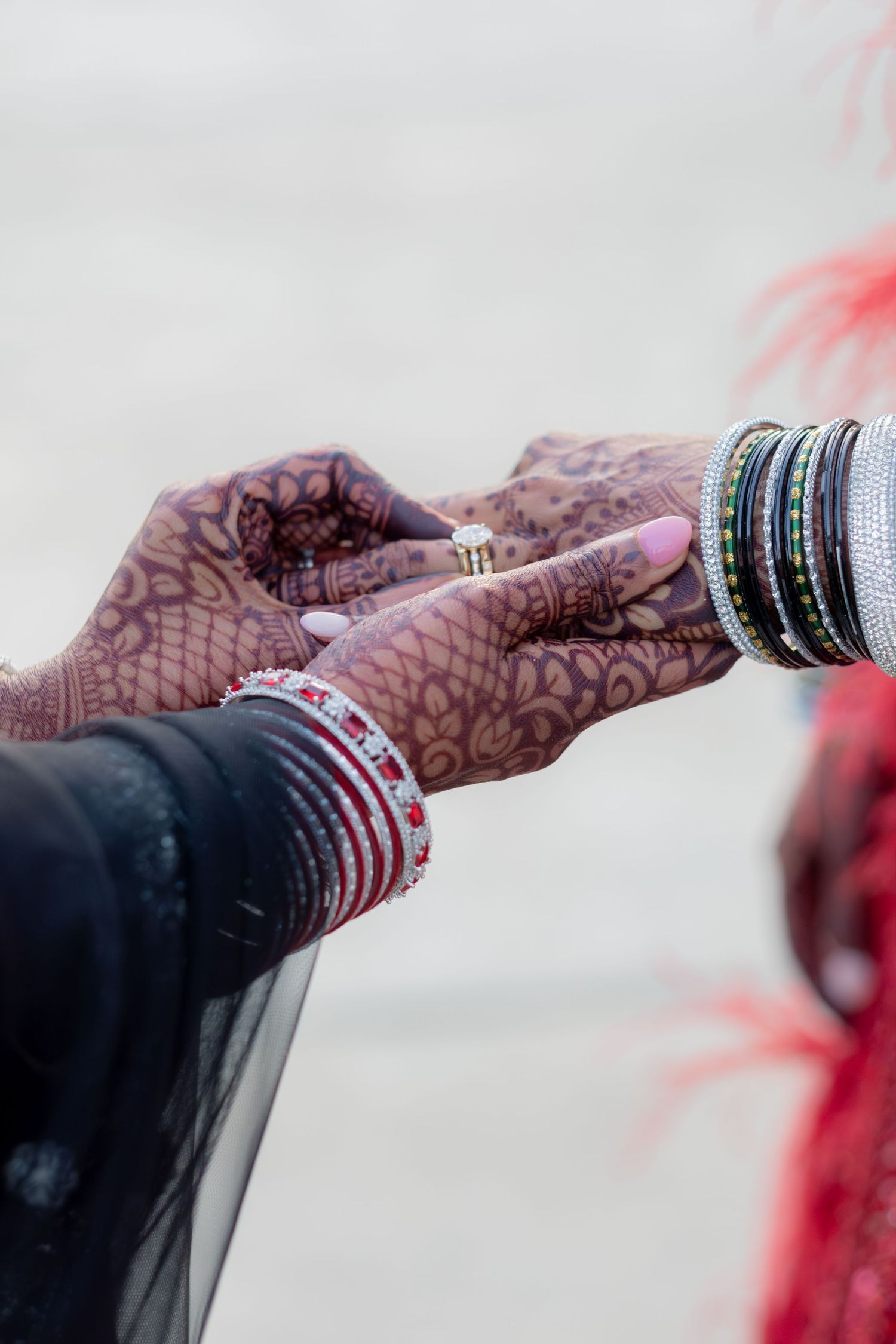 Two hands adorned with henna, bangles, and a ring during an Indian wedding ceremony.