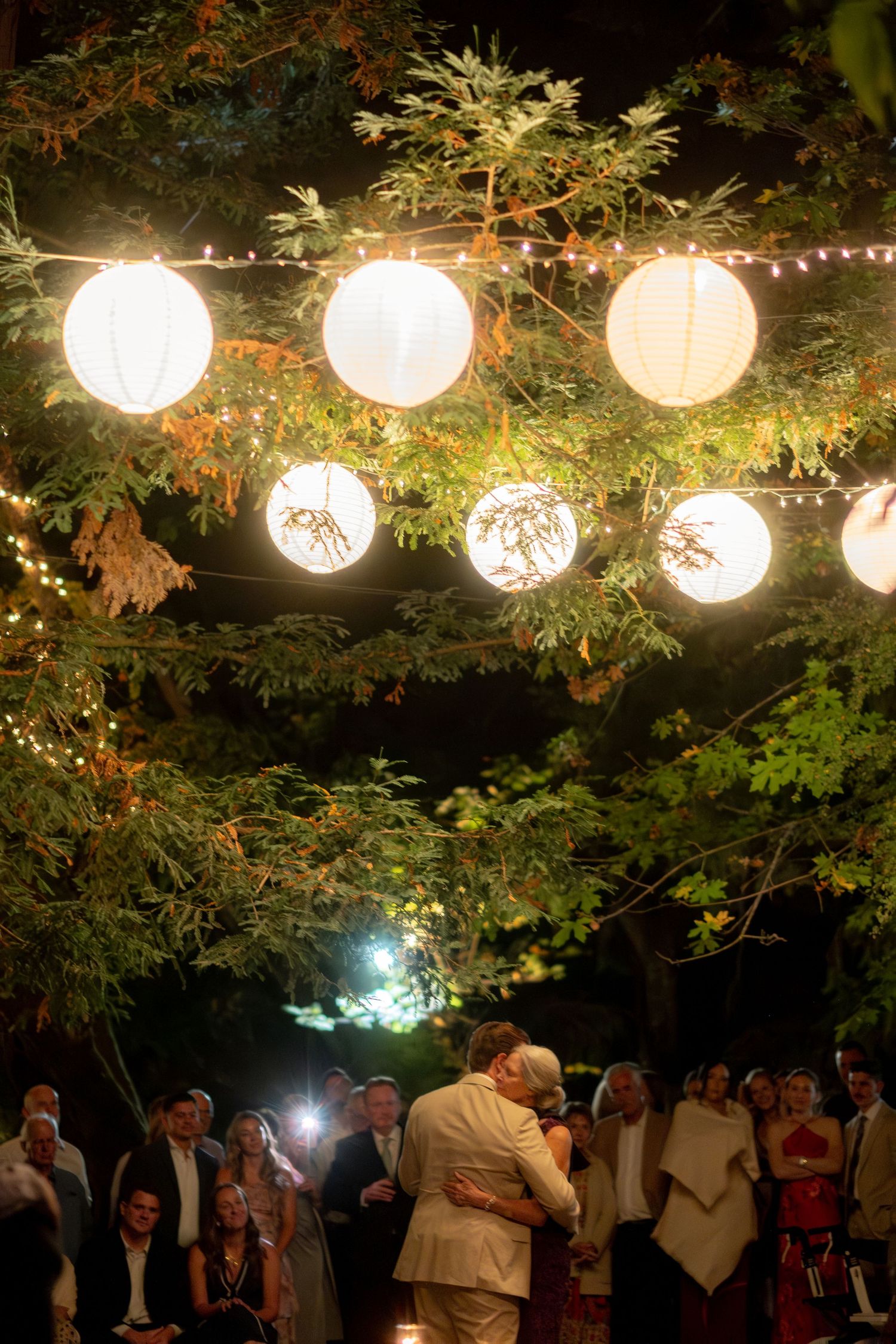 Couple shares first dance under glowing paper lanterns hanging from trees at night wedding.