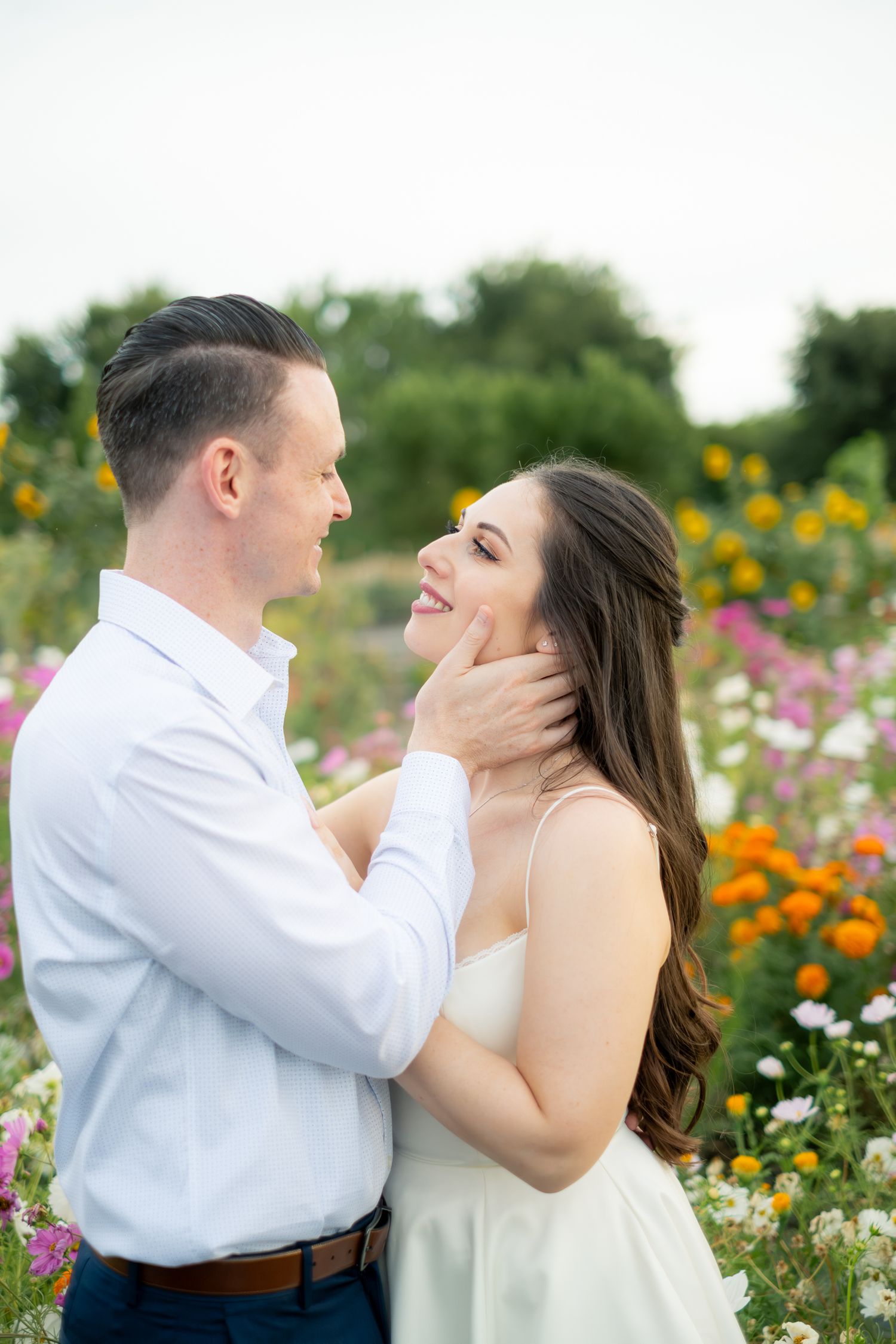 Couple embracing in a colorful flower field, man tenderly holding womans face as they smile at each other.