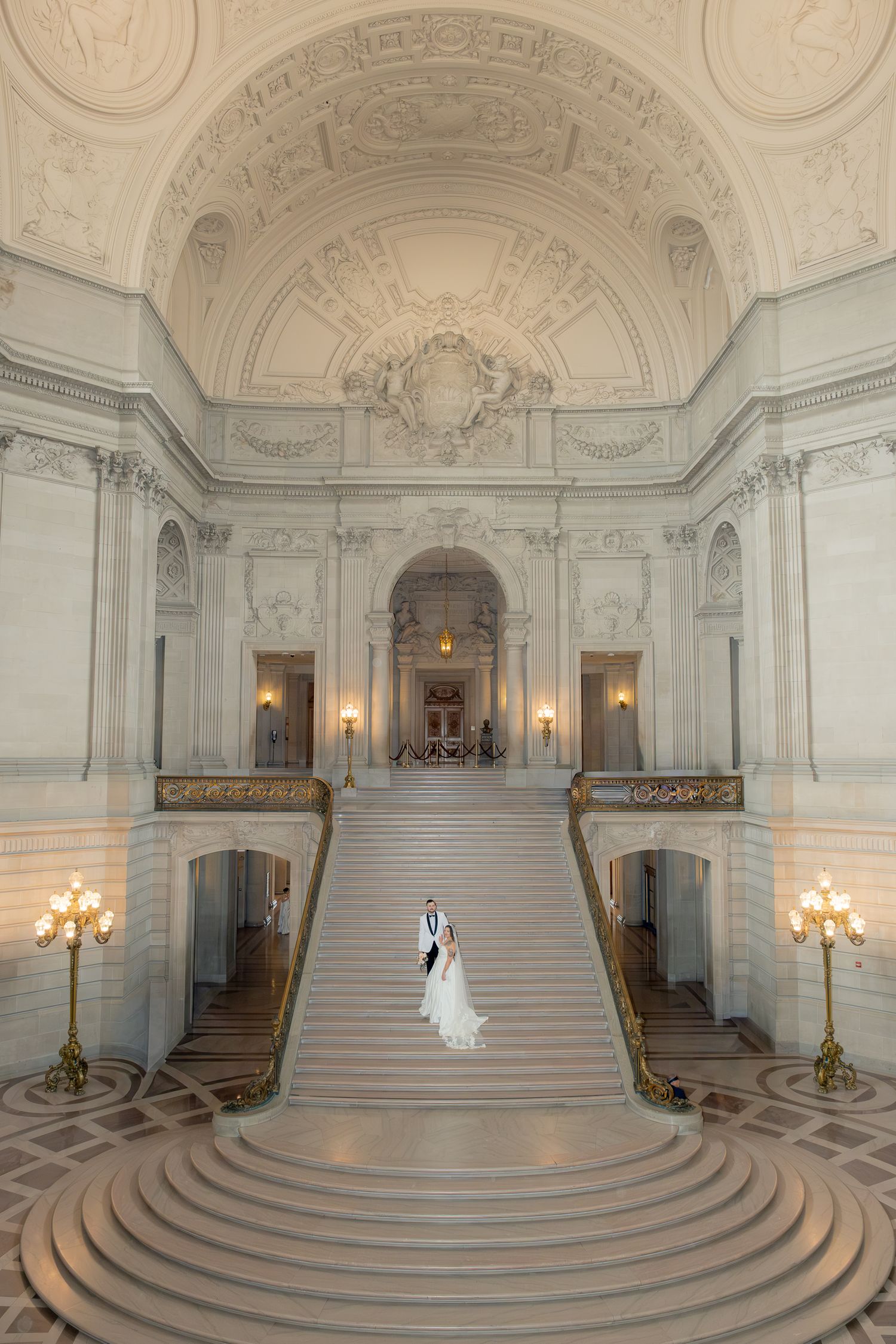 Bride and groom embracing on grand marble staircase inside stunning San Francisco City Hall rotunda.