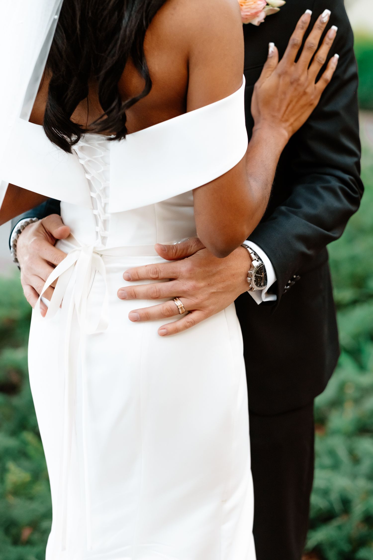 Close-up of groom embracing bride in a lace-back off-shoulder white wedding gown.