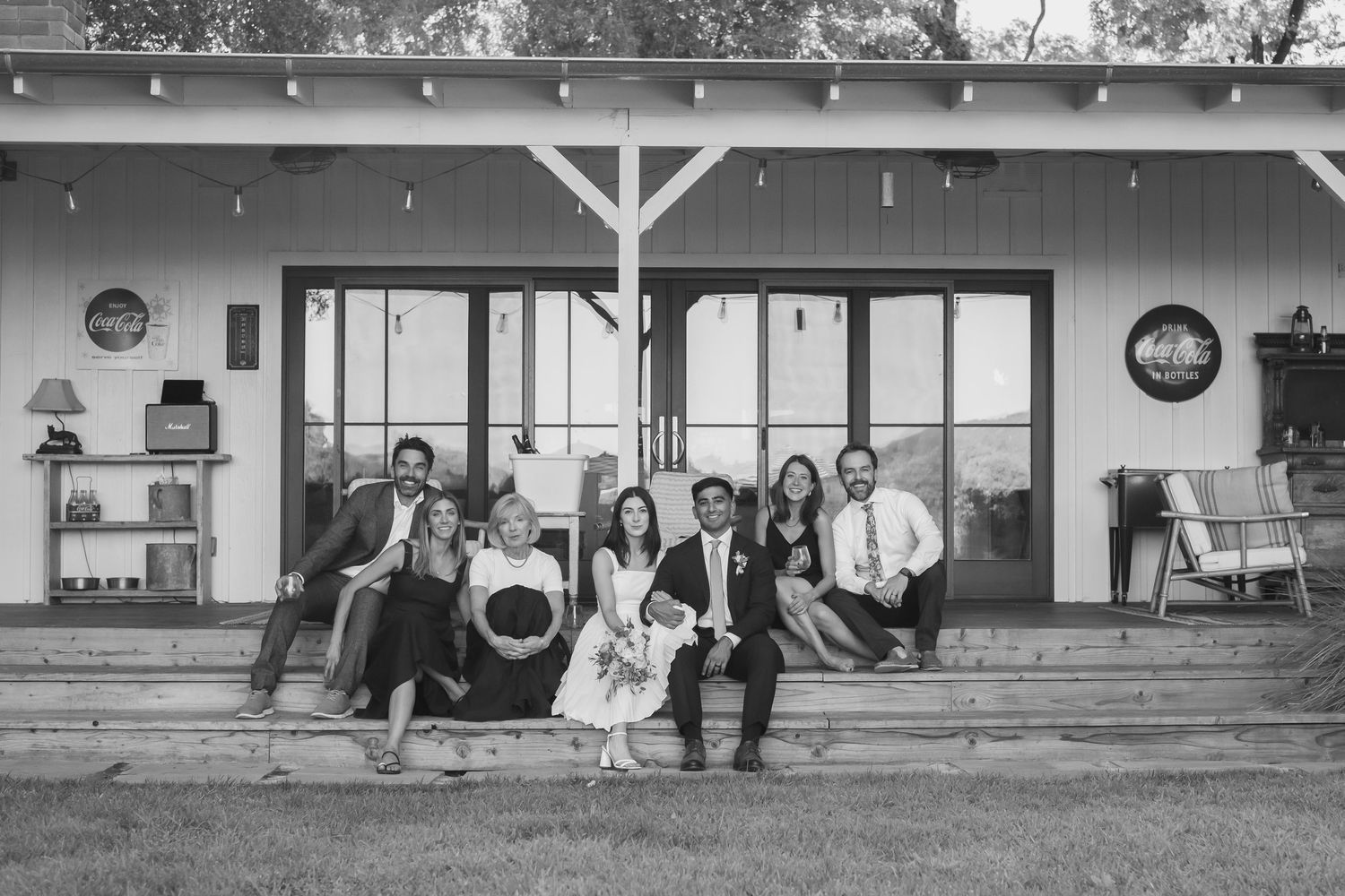Black and white photo of a family group posing on porch steps outside a white farmhouse building.