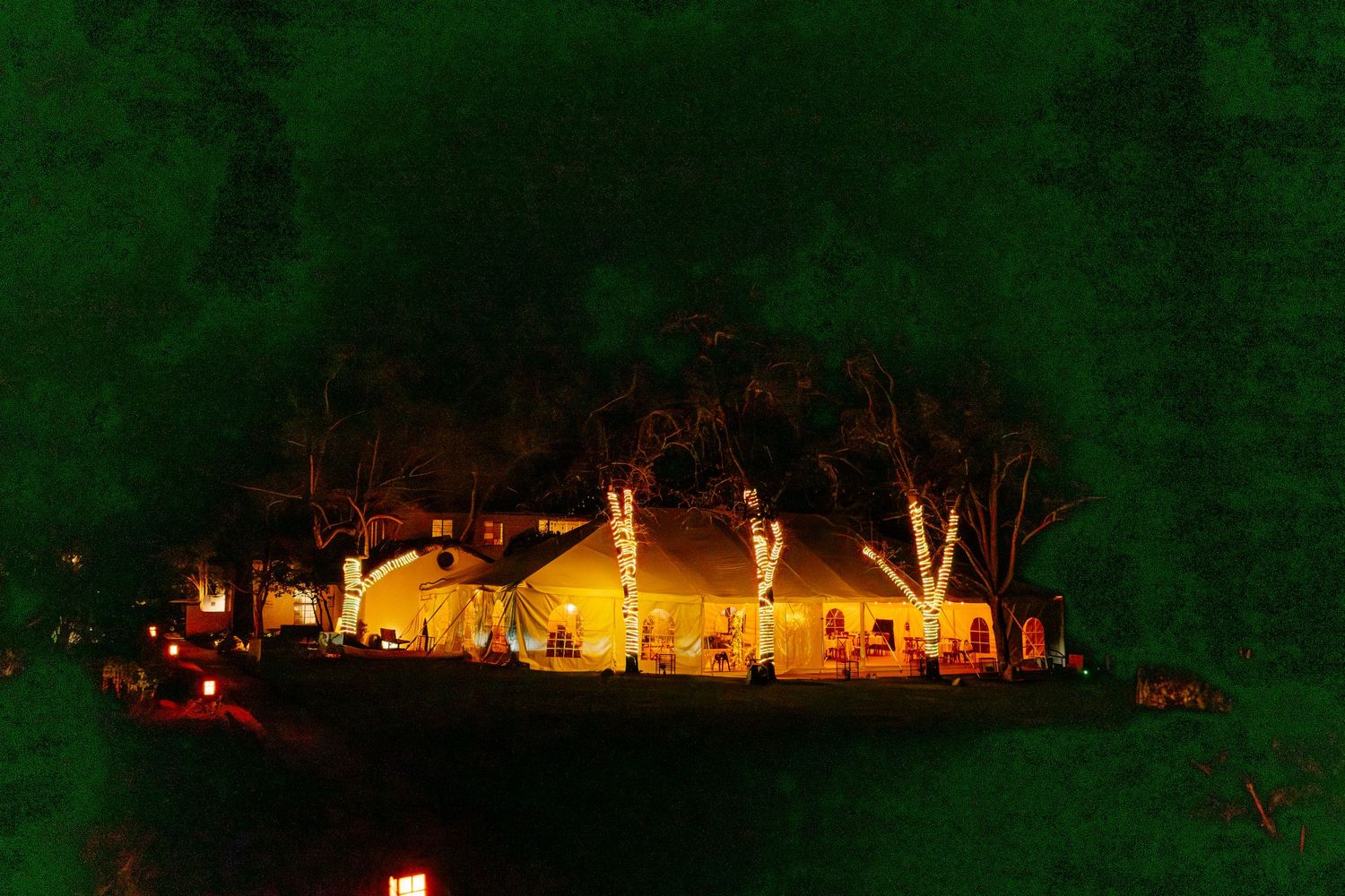 Aerial night view of a warmly lit wedding venue surrounded by illuminated trees outdoors.