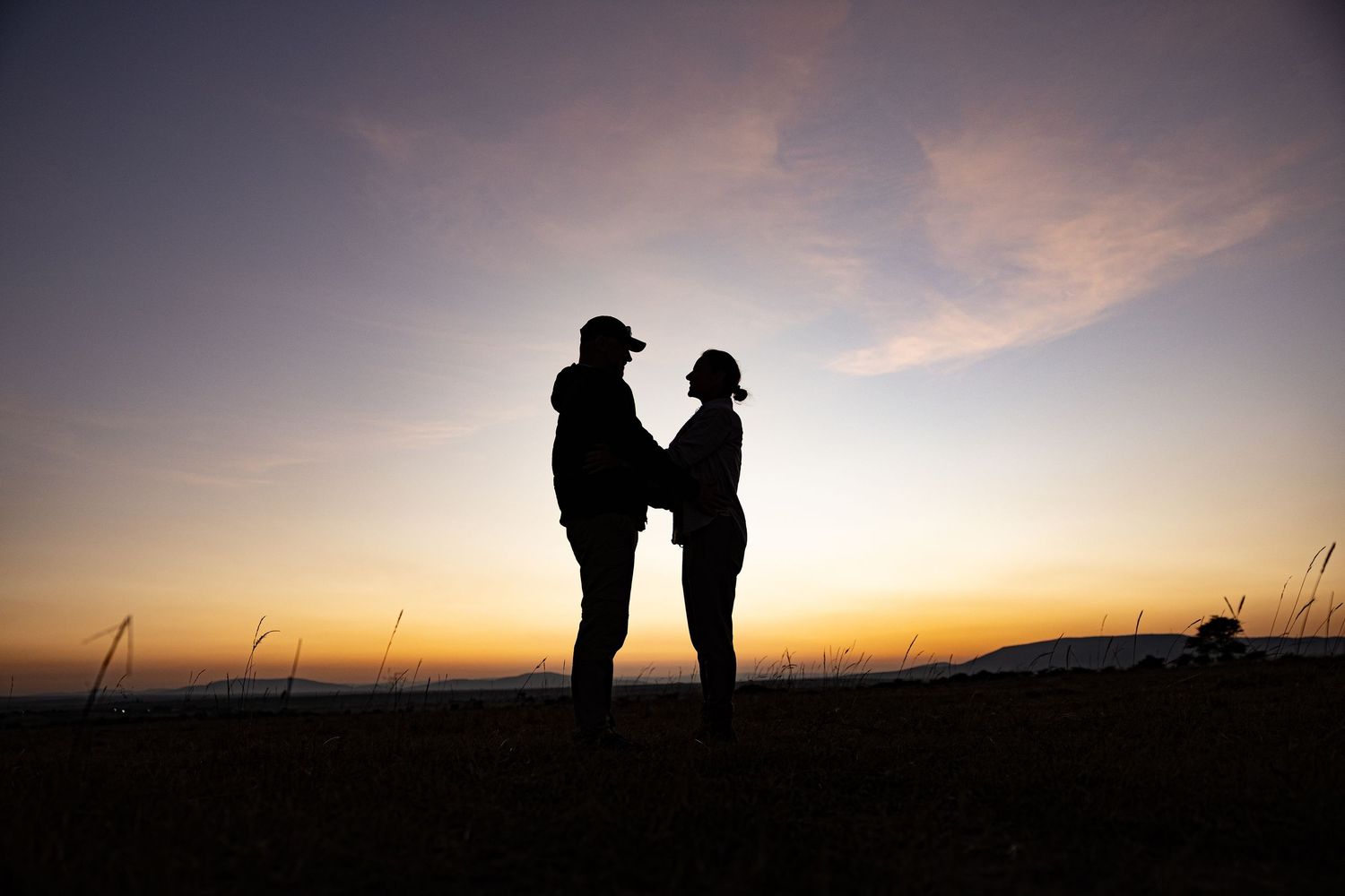 Two figures in silhouette share an intimate moment against a vibrant sunset backdrop.