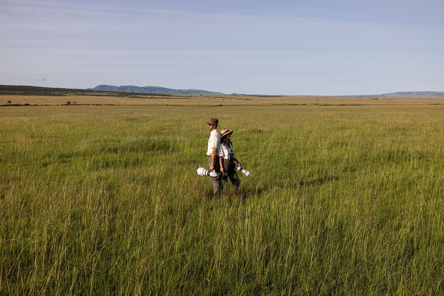 Person walking through vast green marshland with mountains visible on the horizon under a clear blue sky.