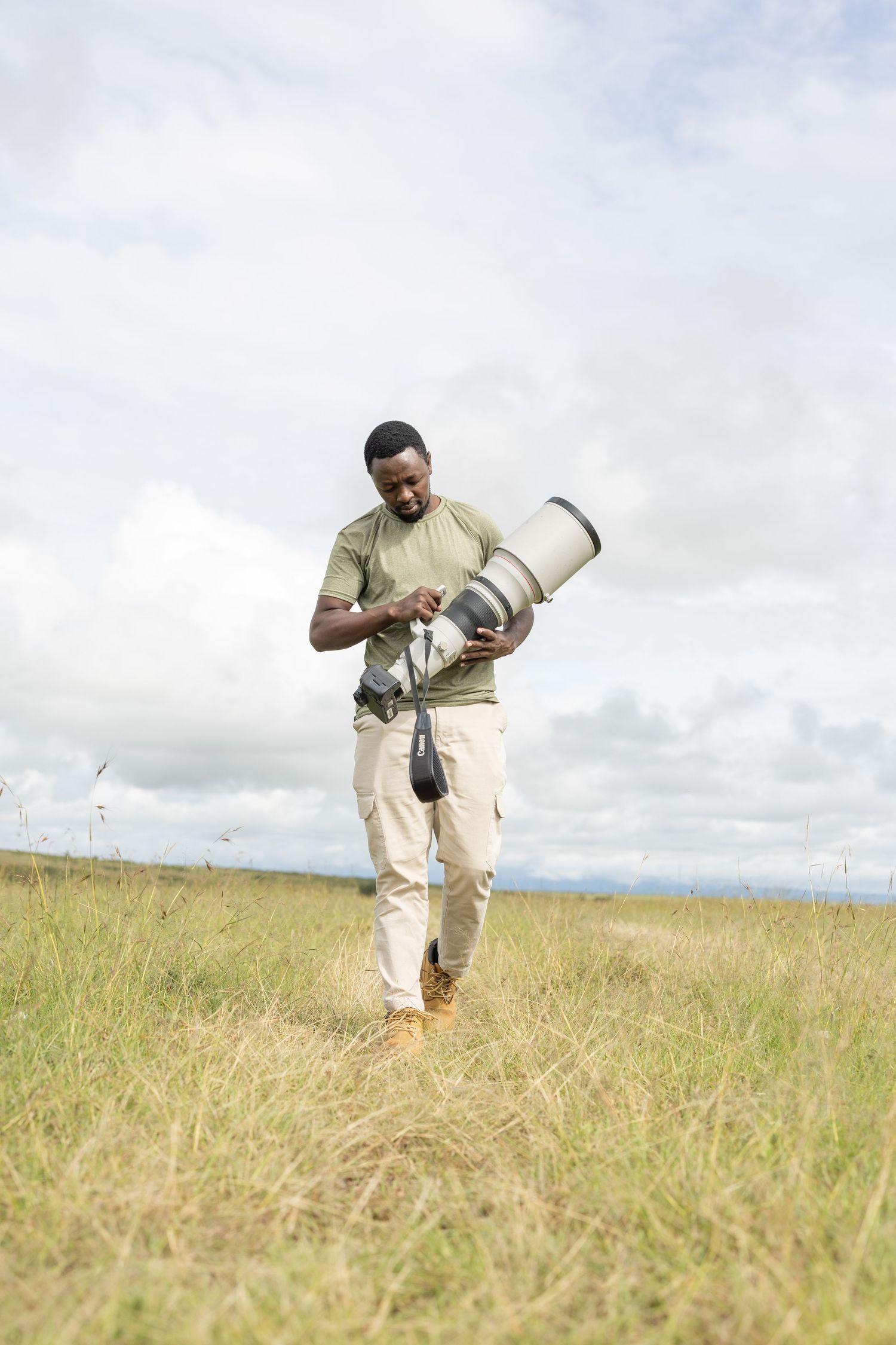 A photographer captures wildlife shots while crouching in tall savanna grass.