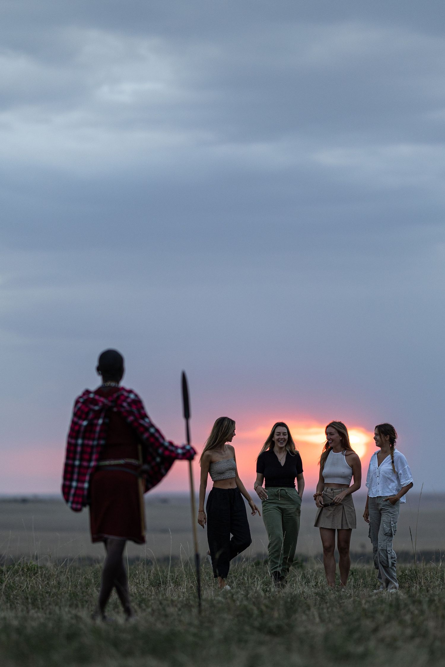 Group of people gathered in a field during a dramatic purple sunset.