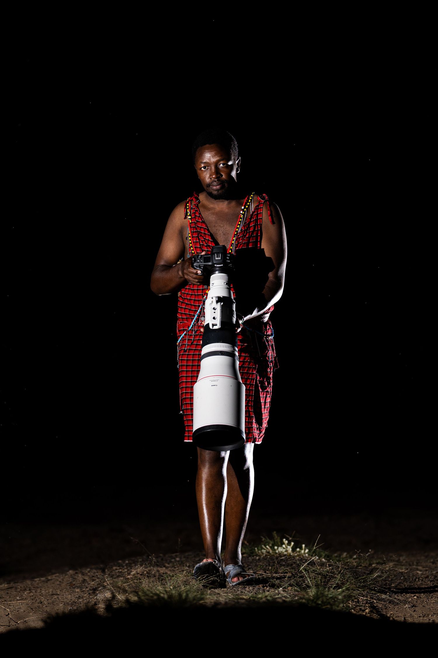 A person in a red plaid shirt stands in darkness holding a large white camera lens at different angles.