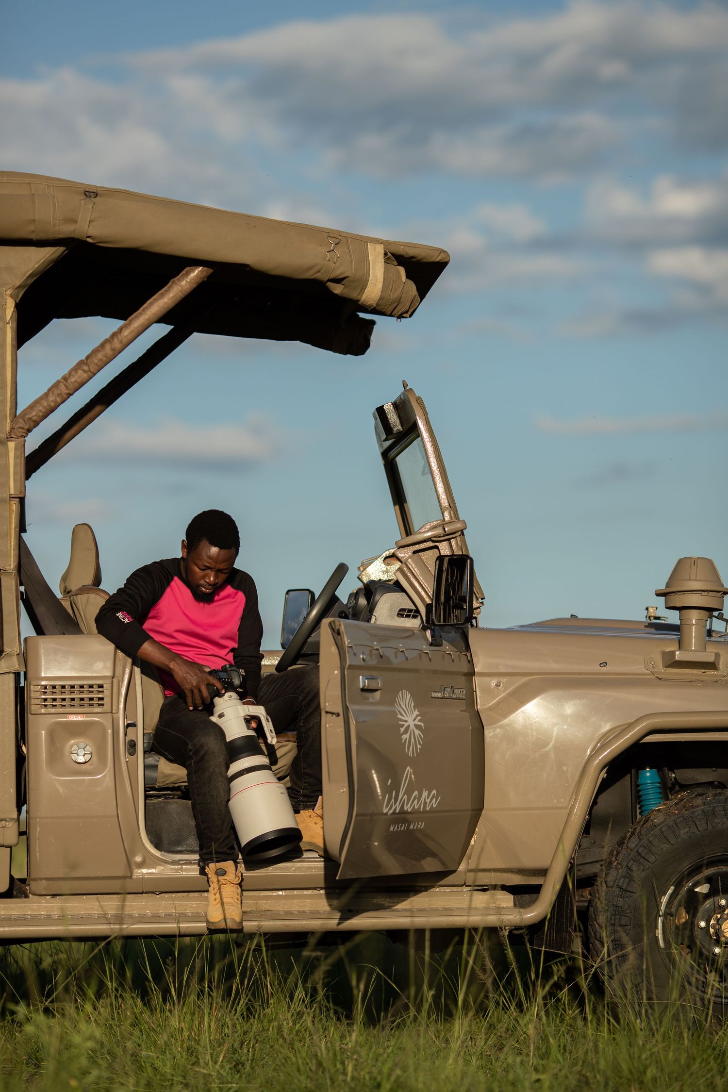 A photographer sits in safari vehicle with professional camera gear during wildlife shoot.