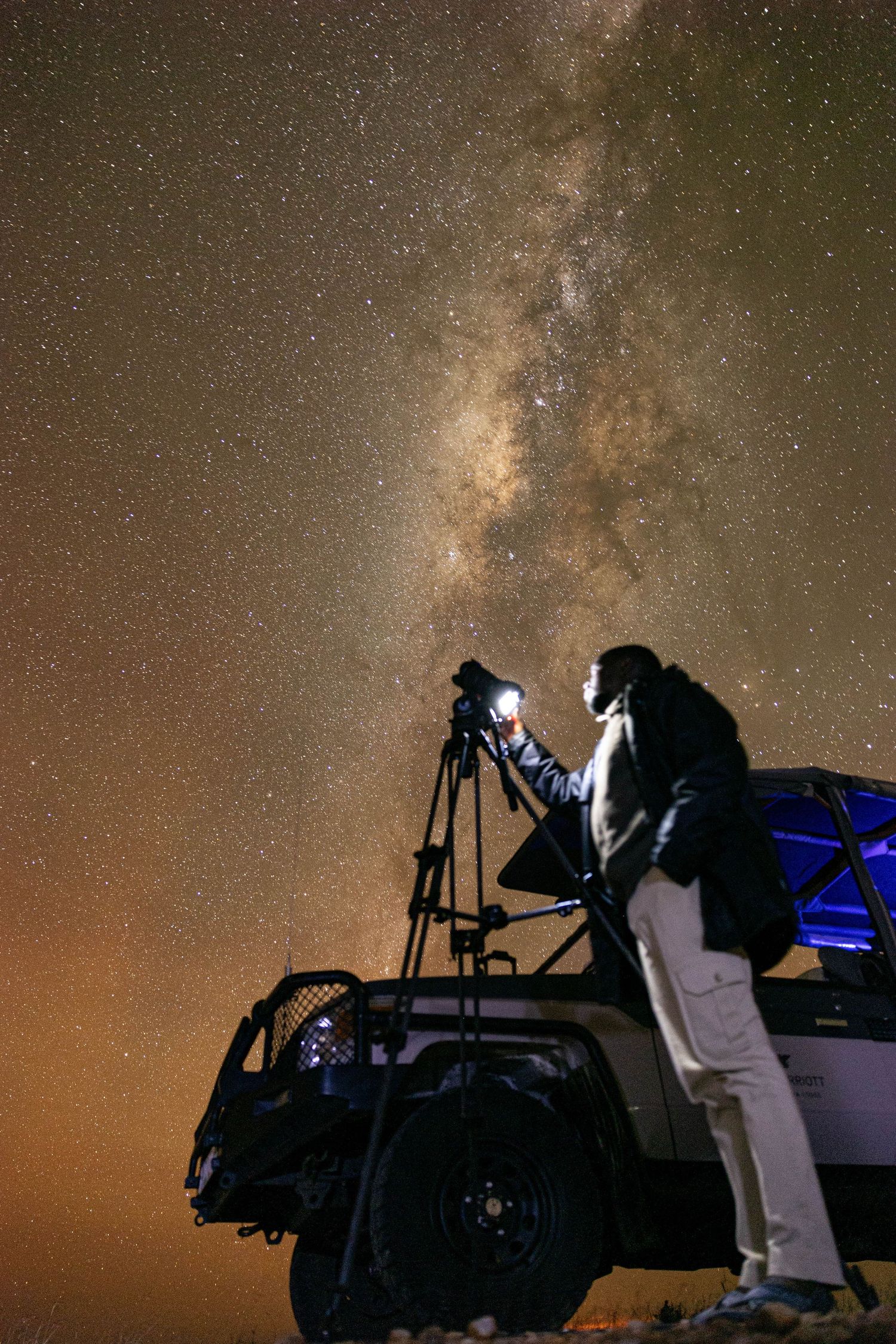 Silhouette of photographer capturing the Milky Way while standing on vehicle at night.