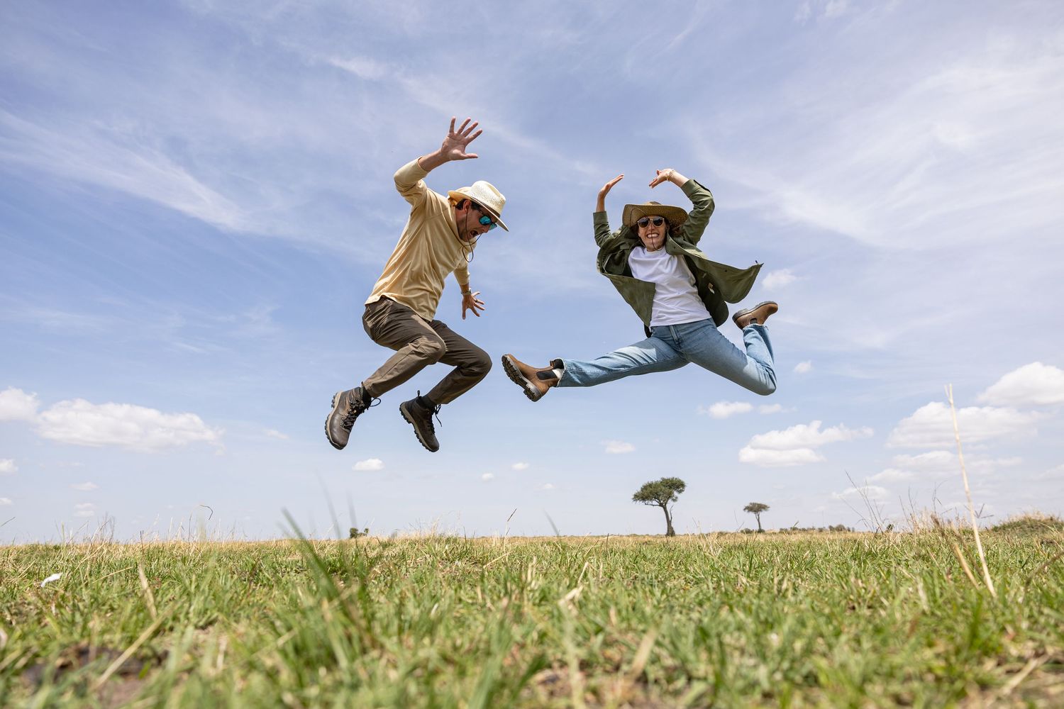 Two joyful people jumping high in the air on a green grassy field under a bright blue sky.