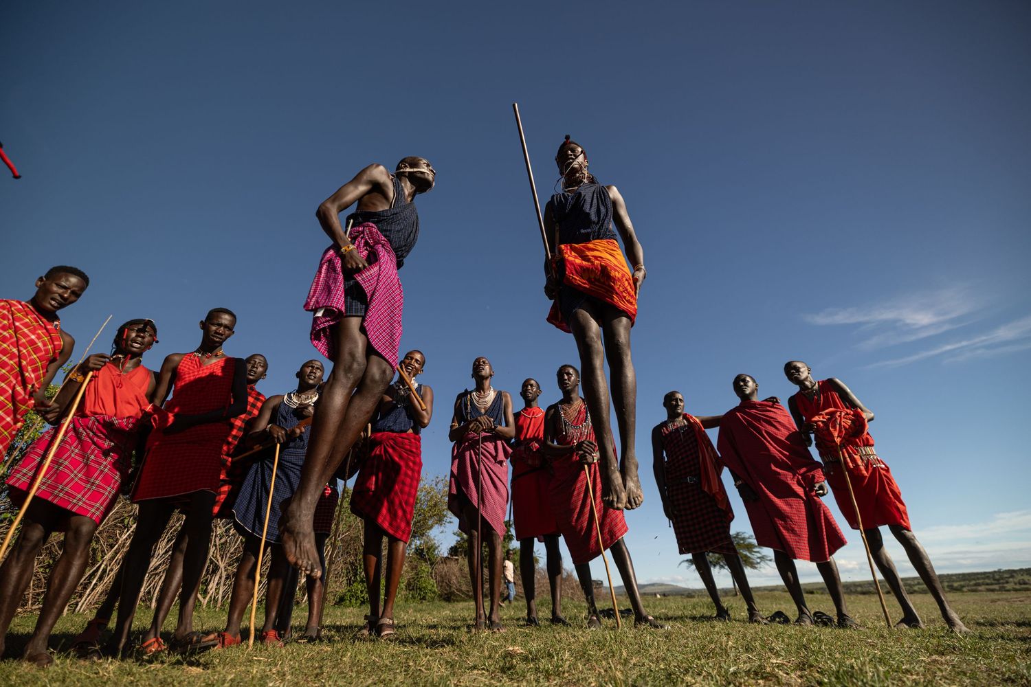 Maasai warriors performing traditional jumping dance in colorful red robes against a clear blue sky in Africa.