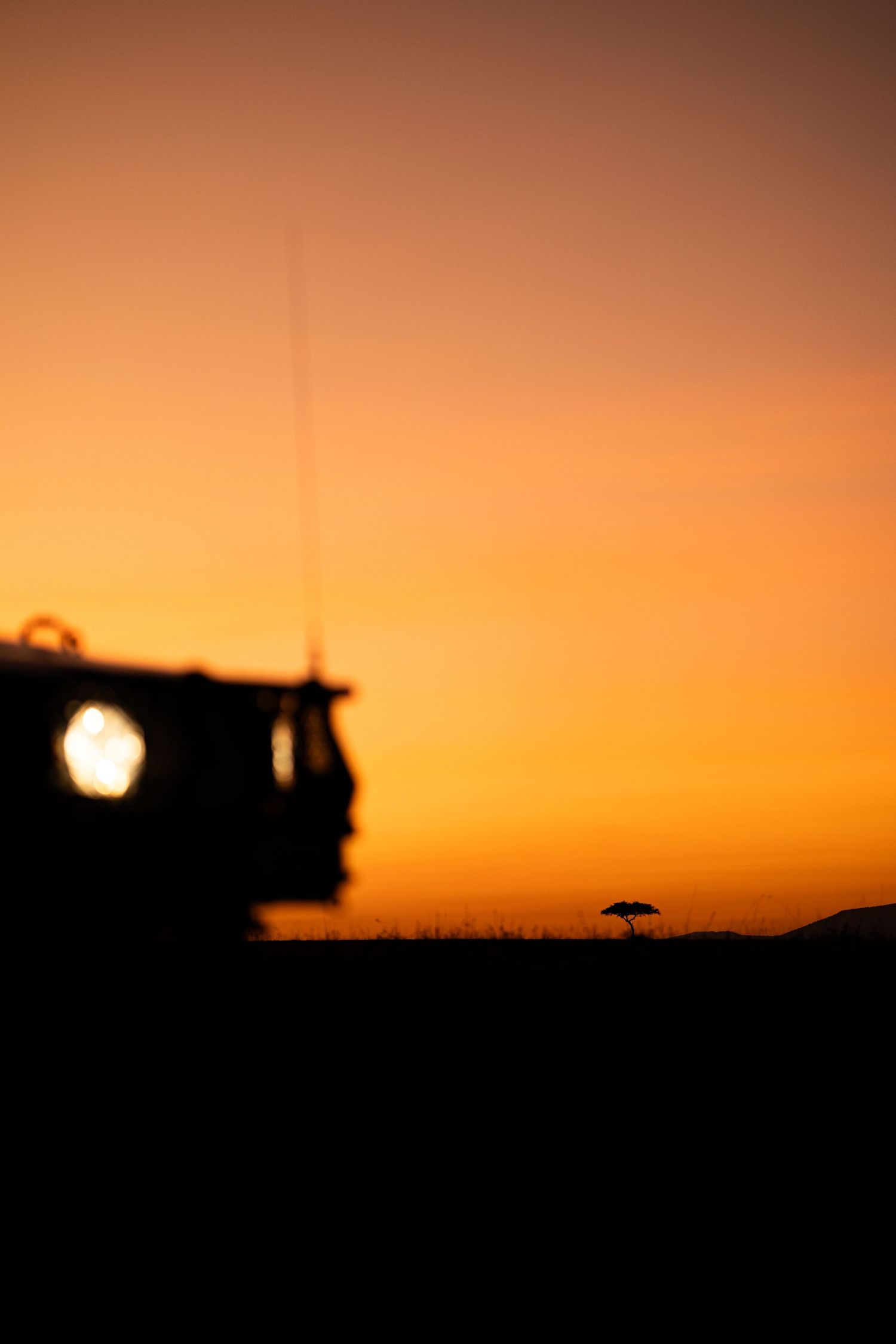 Safari vehicle silhouetted against a dramatic orange African sunset.
