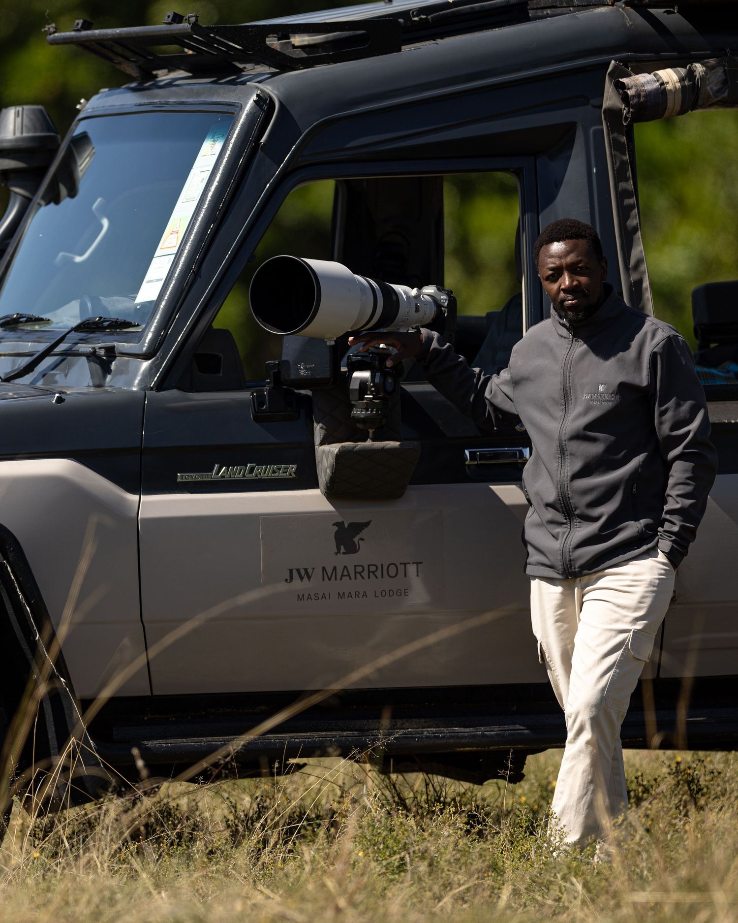 Safari vehicle parked in tall grass with JW Marriott branding visible.