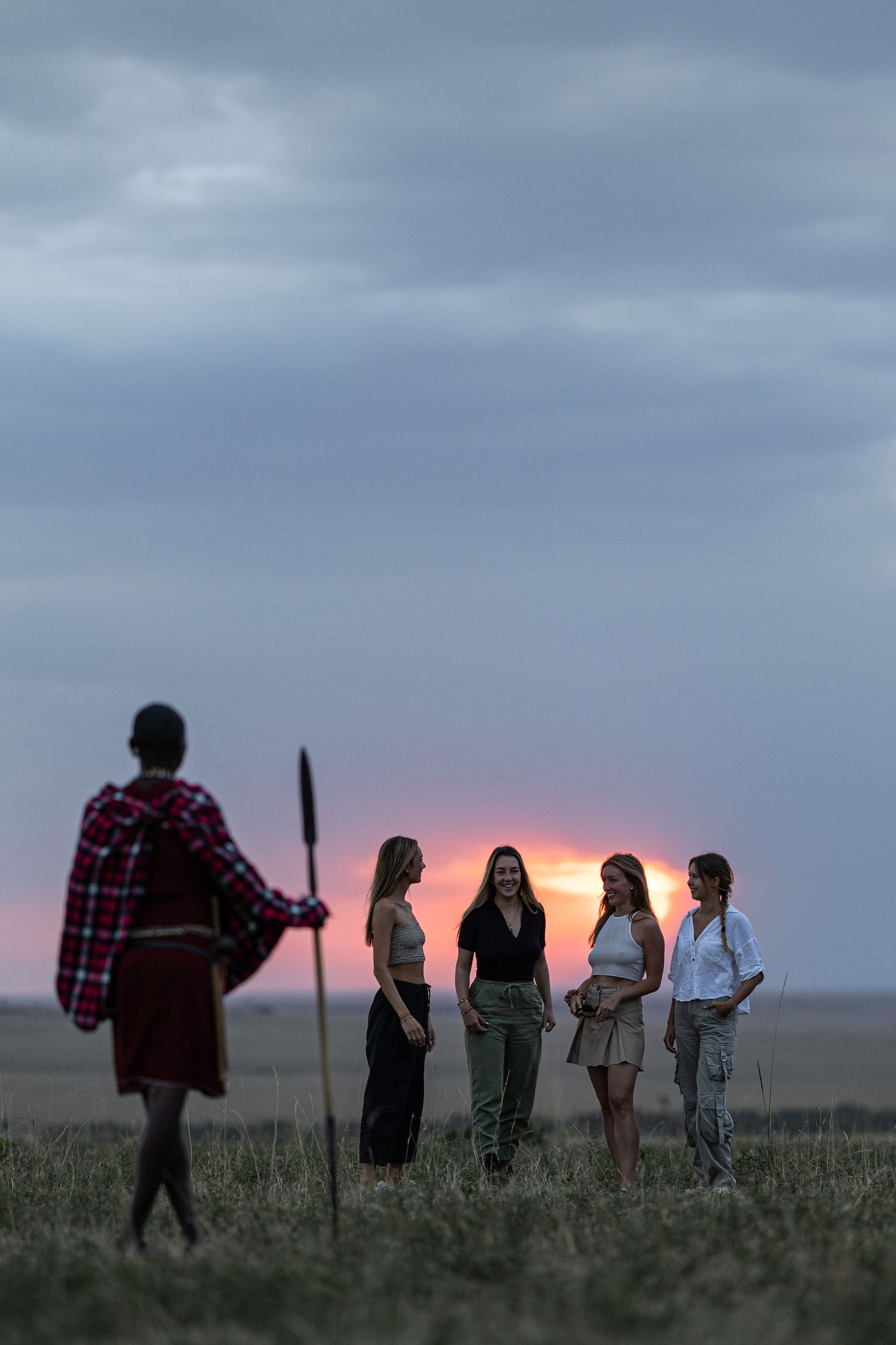 Silhouettes of people standing together against dramatic sunset sky in open field.