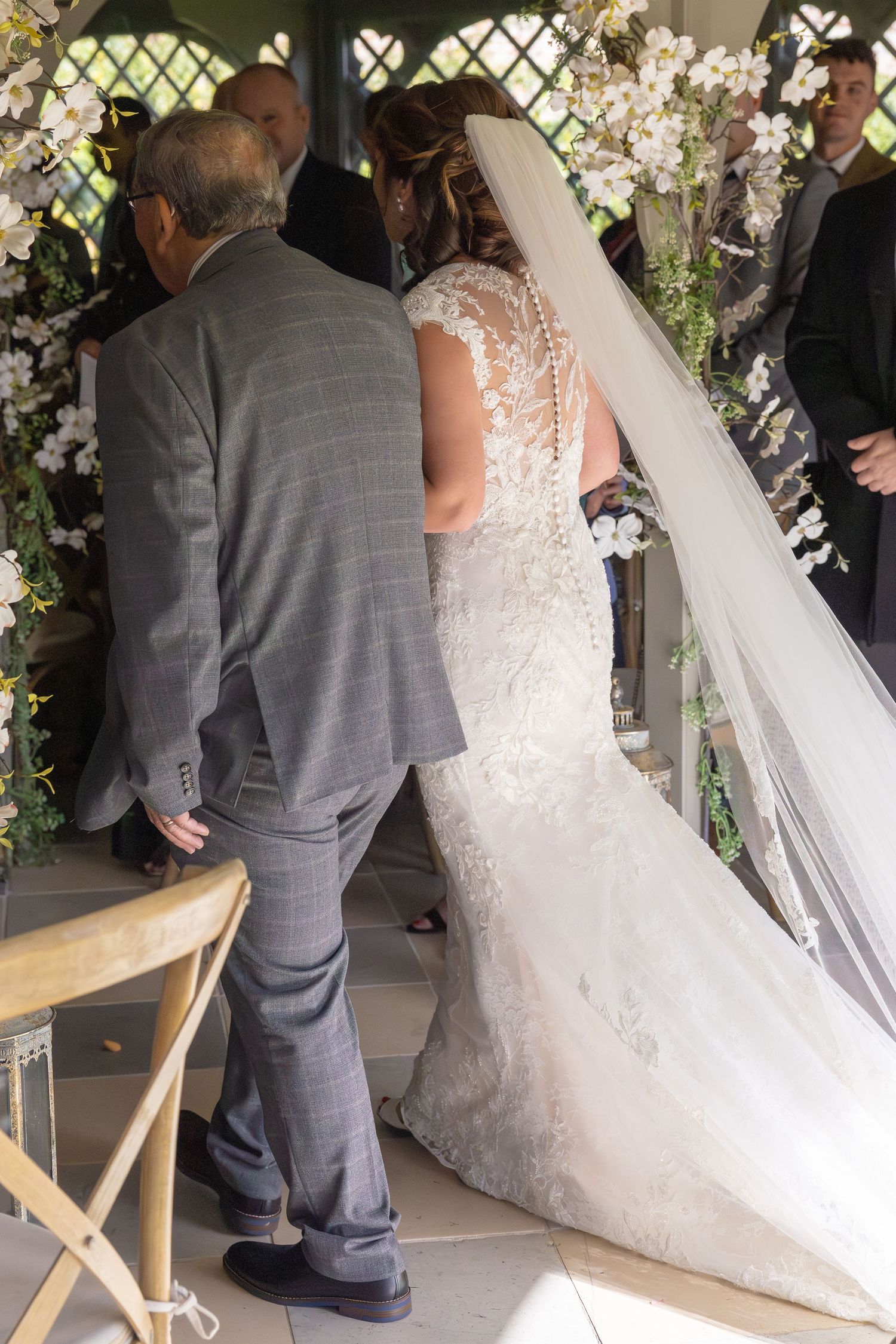 A series of wedding ceremony photos showing a white lace wedding dress and gray suit at an indoor venue with floral decor.