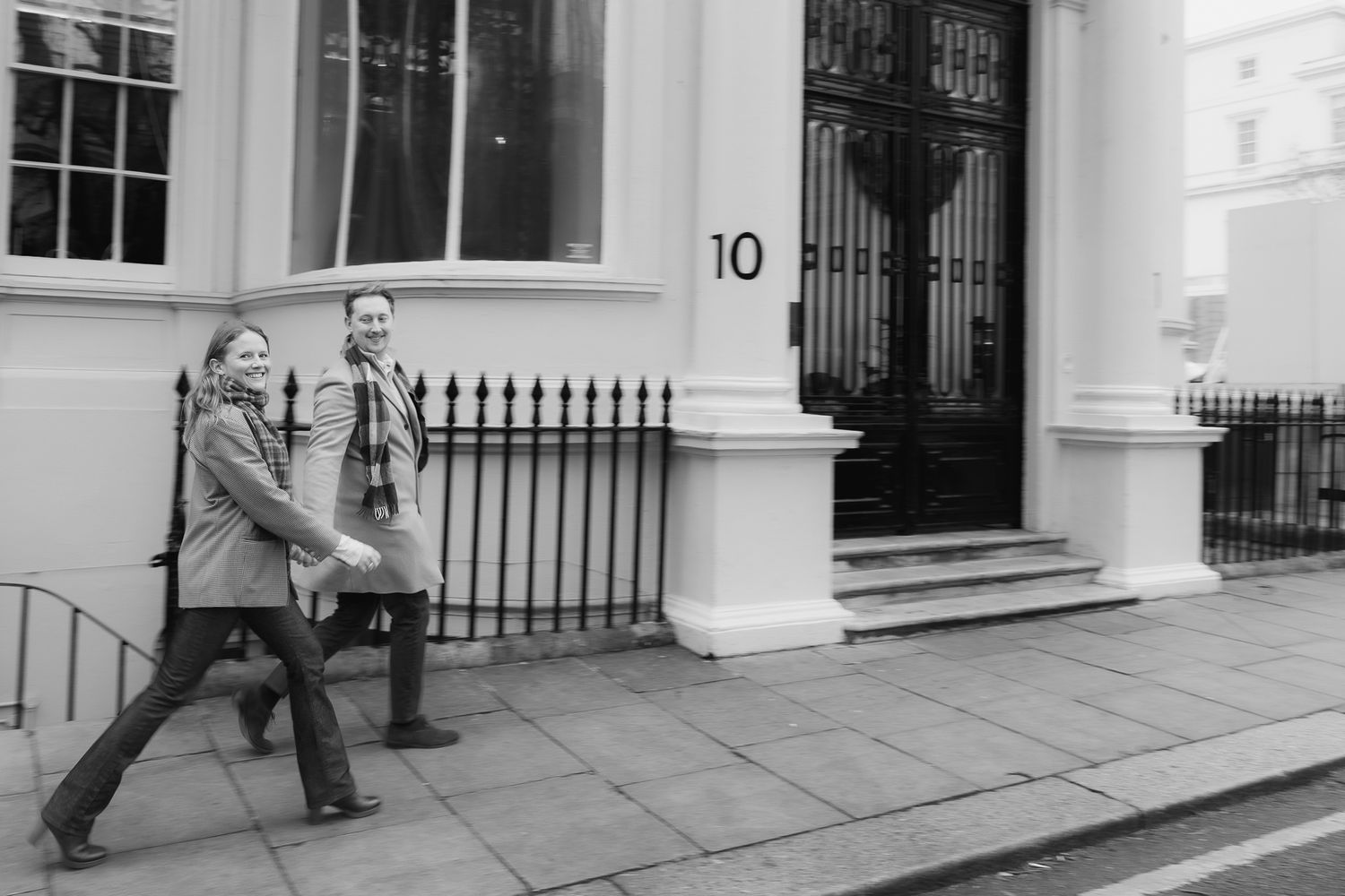 A sequence showing two people in winter coats dancing and spinning on a city sidewalk.