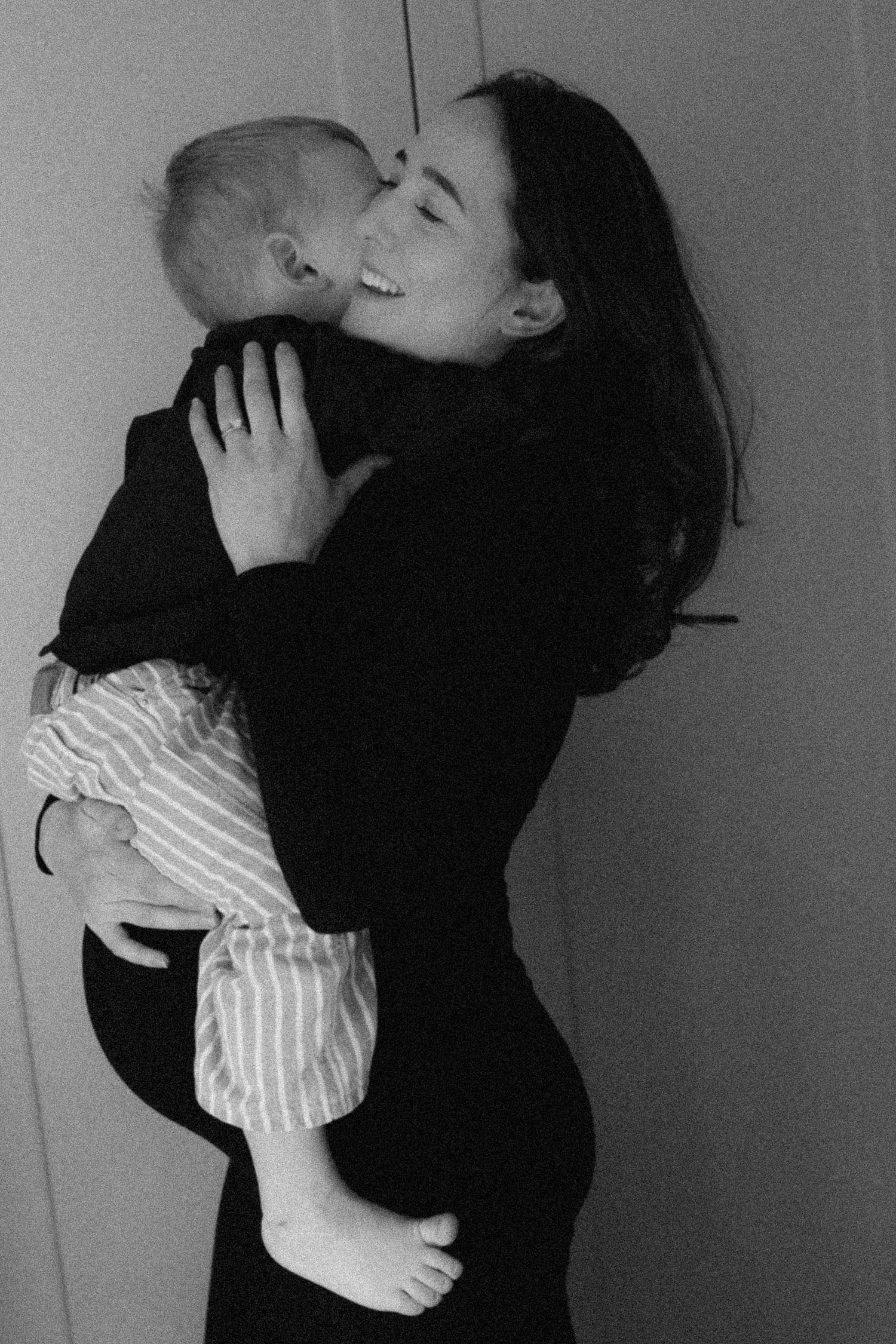 Joyful mother in black dress holding and cuddling infant baby in black and white photo.